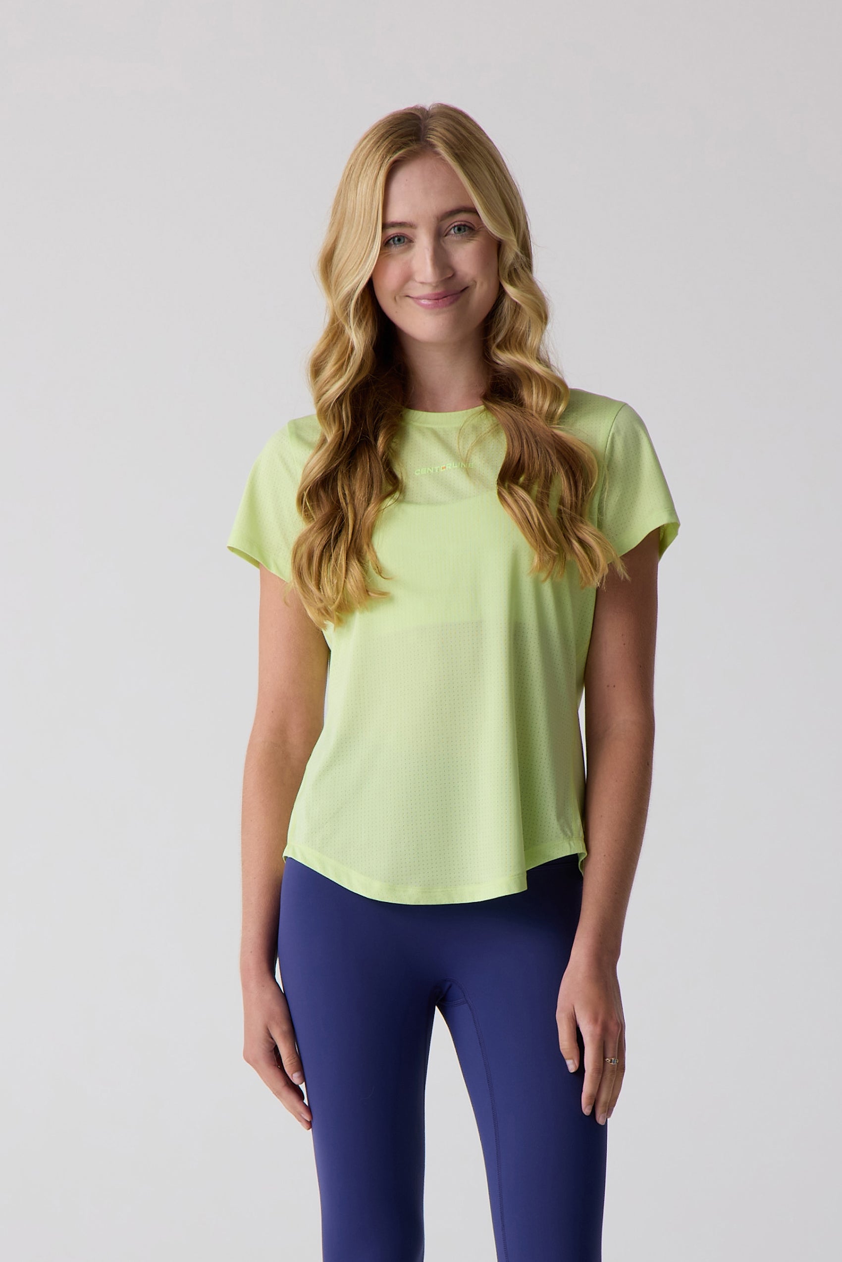 Lime green AirLite short sleeve tee by Centerline Athletics, with a perforated texture and logo on the chest, worn with blue leggings.