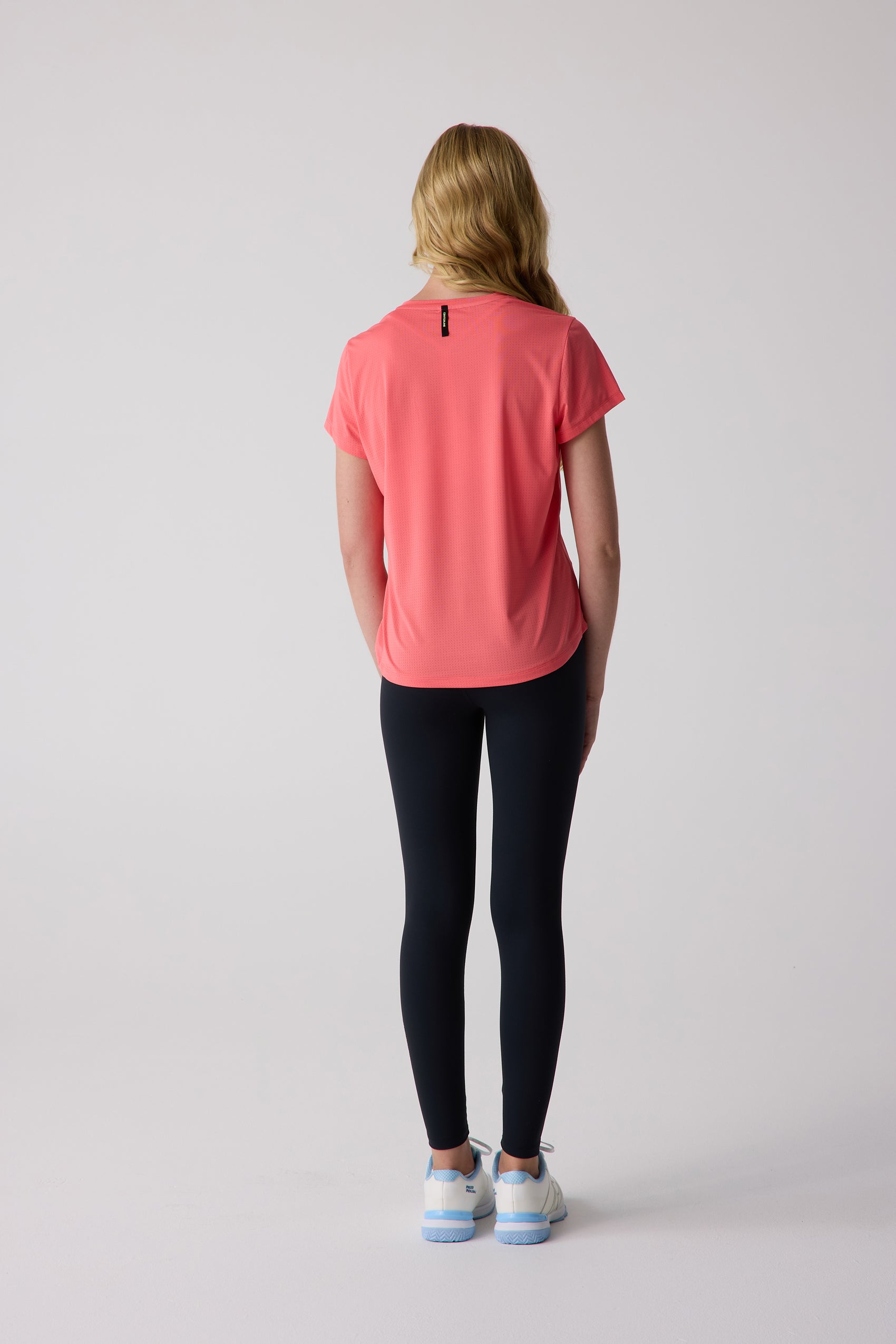 Coral short sleeve tee by Centerline Athletics with perforated knit fabric, worn from the back over black leggings and sneakers.