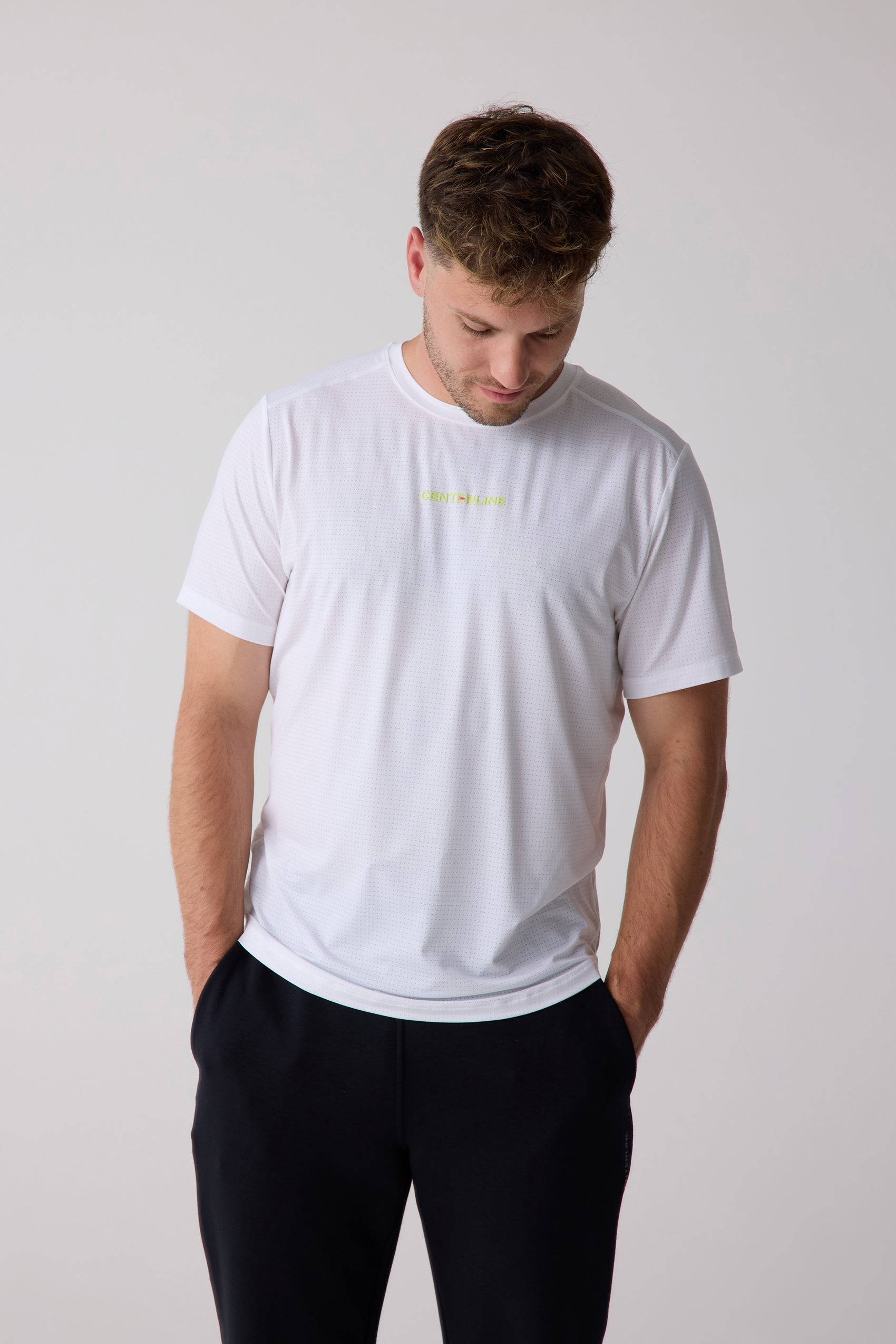 White men's AirLite tee by Centerline Athletics, featuring a perforated texture and lime green chest logo, worn with black pants.