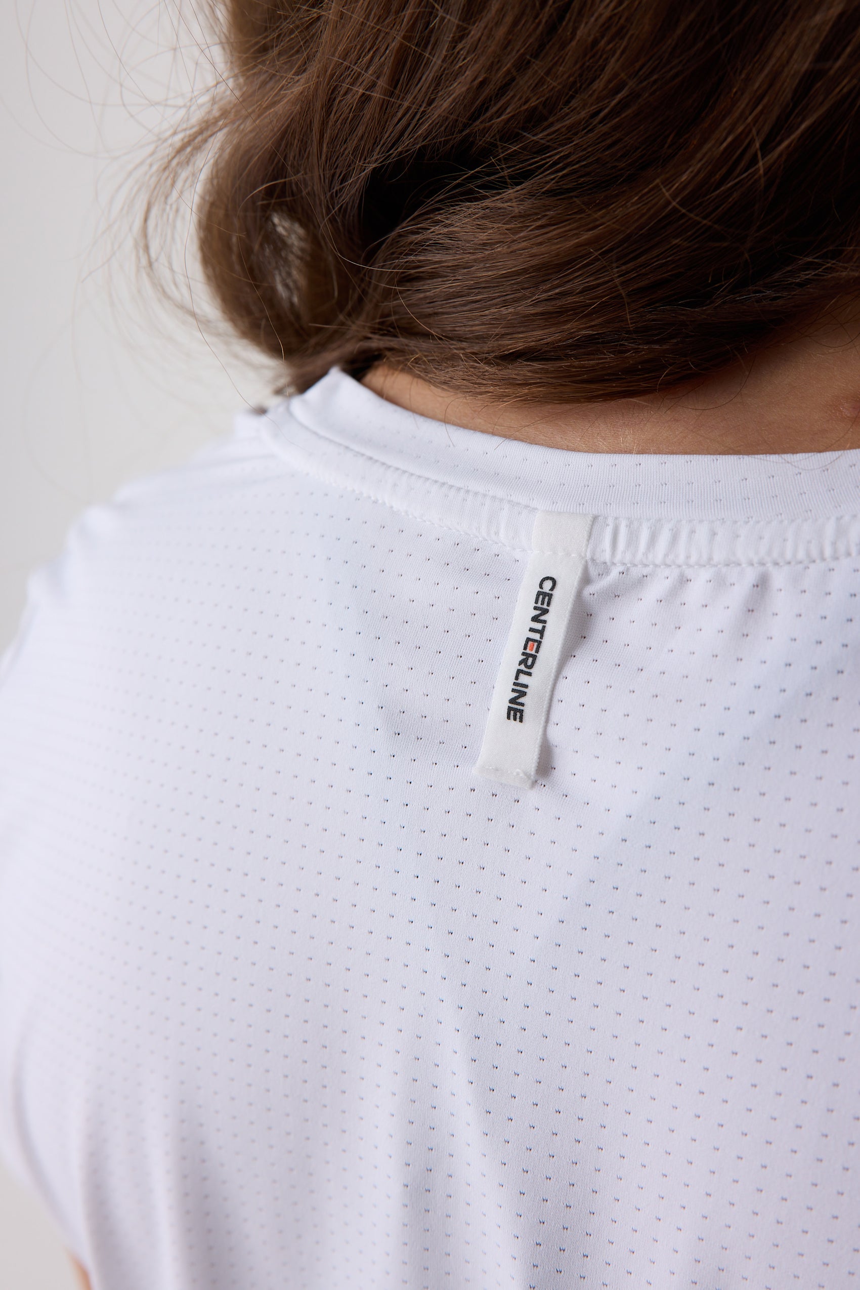 White perforated women's tee by Centerline Athletics, with a vertical "CENTERLINE" tag at the back neck.