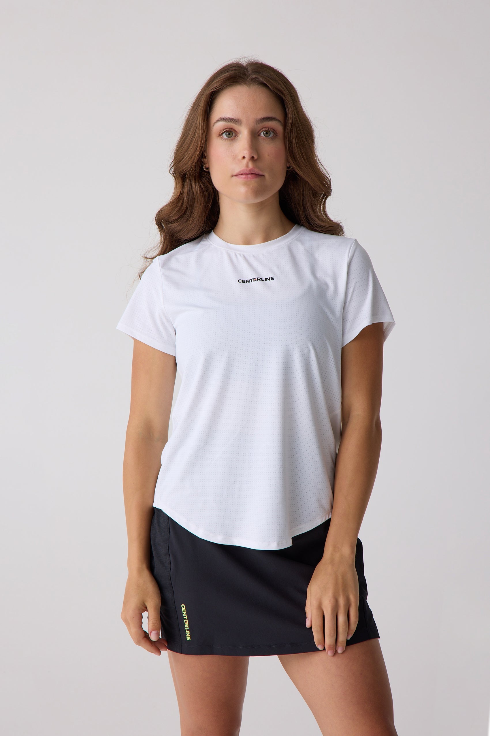 White perforated women's short sleeve shirt by Centerline Athletics with a black logo, worn by a model with a black skirt.