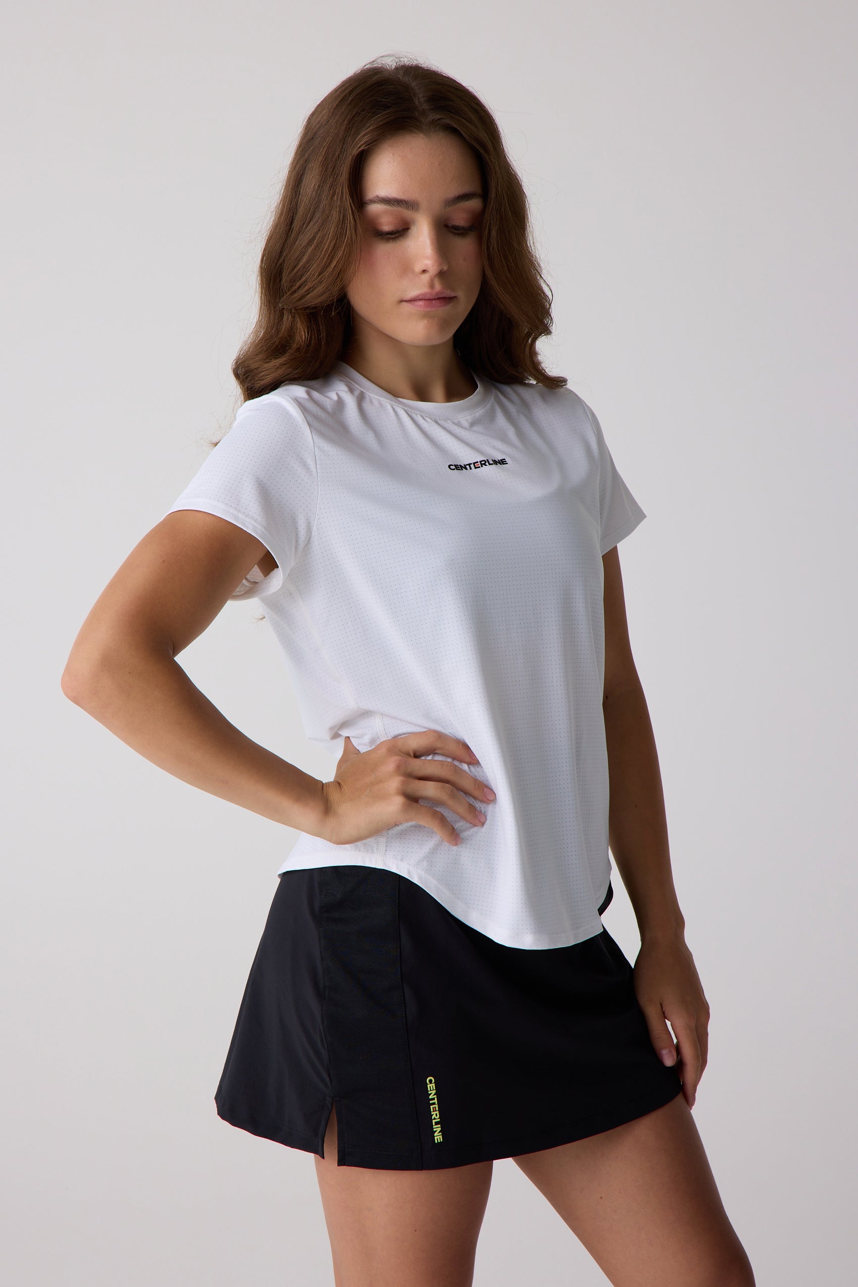 White perforated Women's AirLite Tee by Centerline Athletics with logo on chest, worn with a black skirt.
