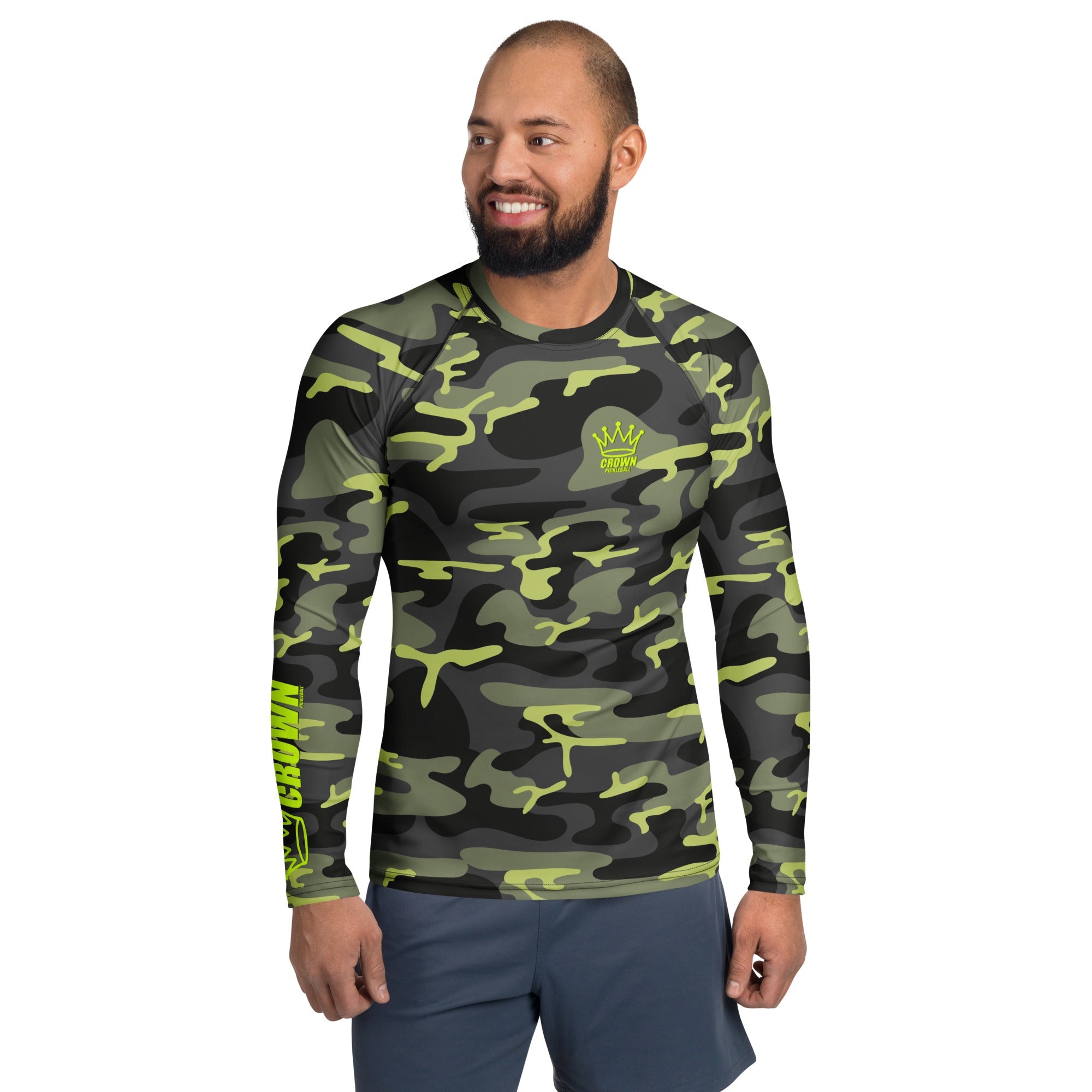 Man in camouflage long-sleeve rash guard with "Crown Pickleball" logo and blue shorts, smiling.

