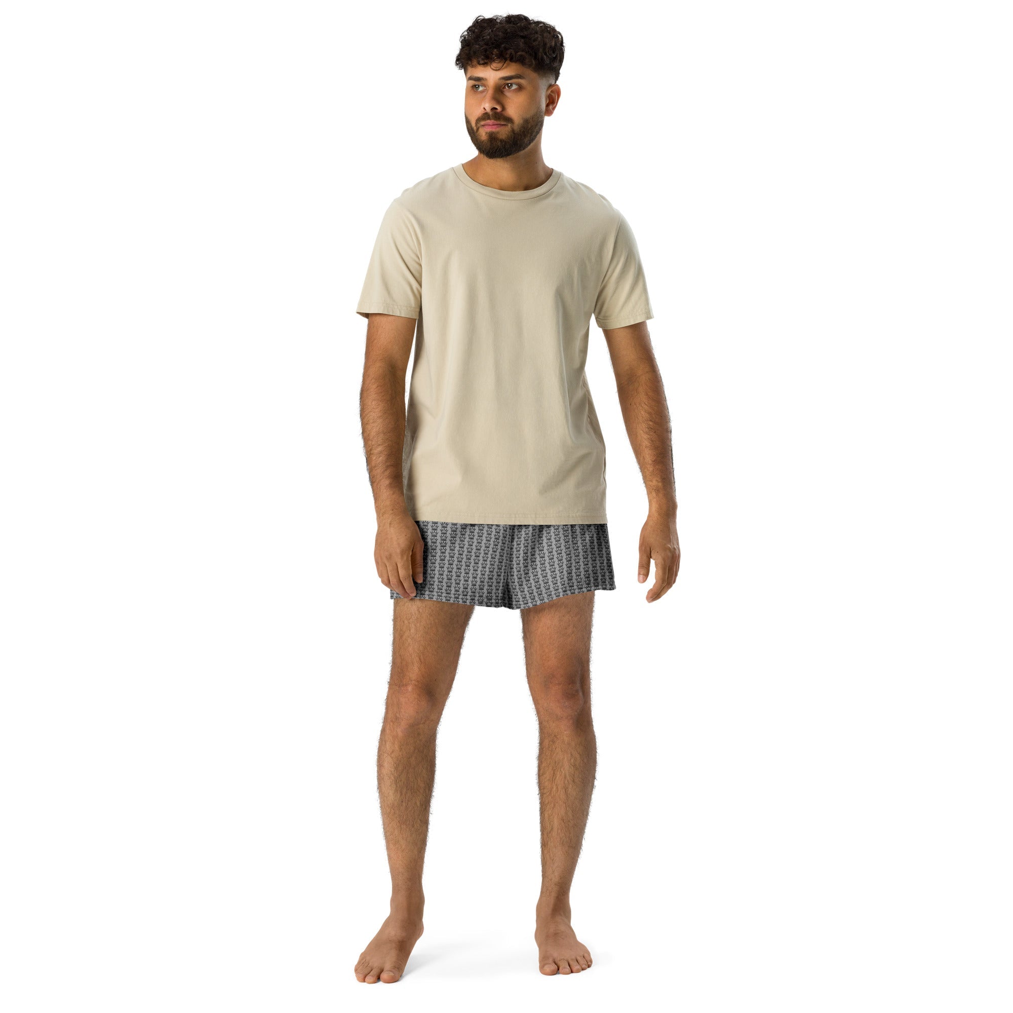 Man in a beige T-shirt and patterned boxer shorts, standing barefoot.