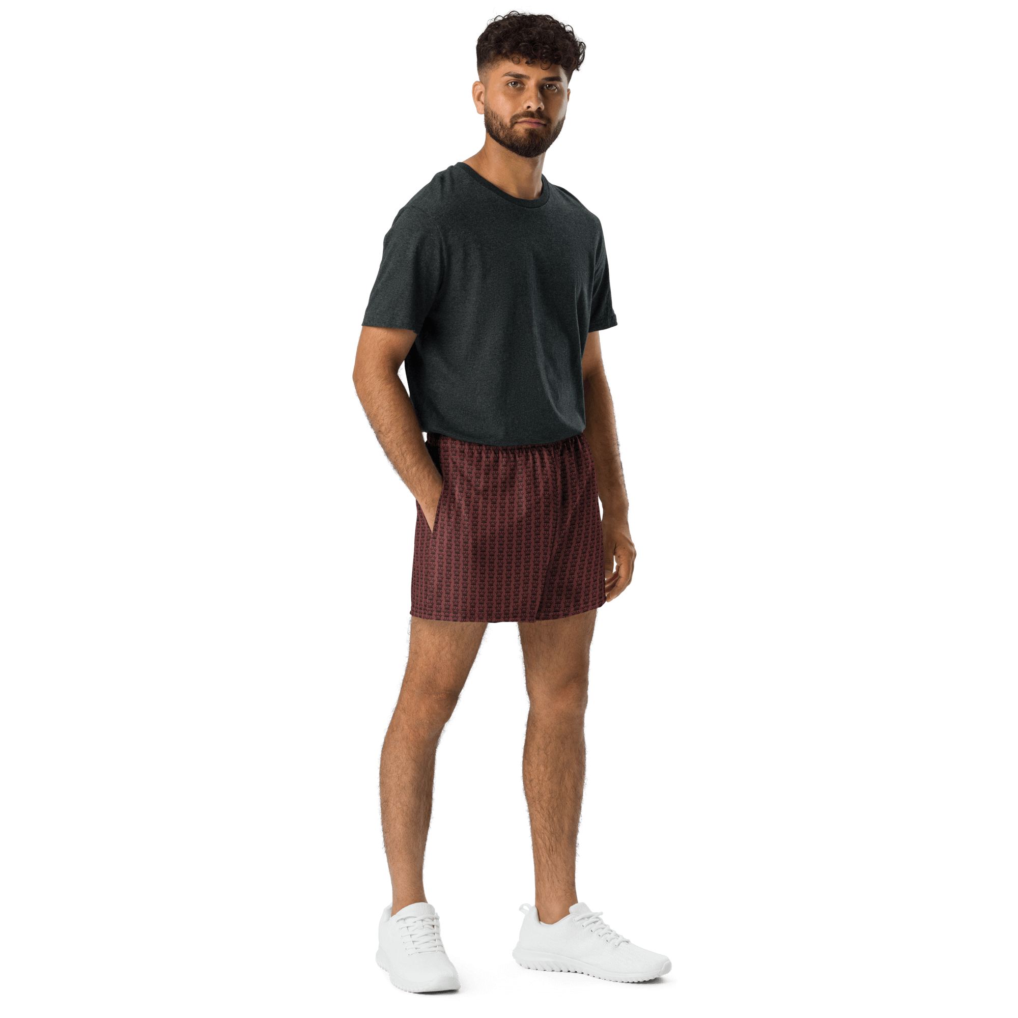 A man wearing a gray t-shirt, patterned maroon shorts, and white sneakers, standing against a black background.