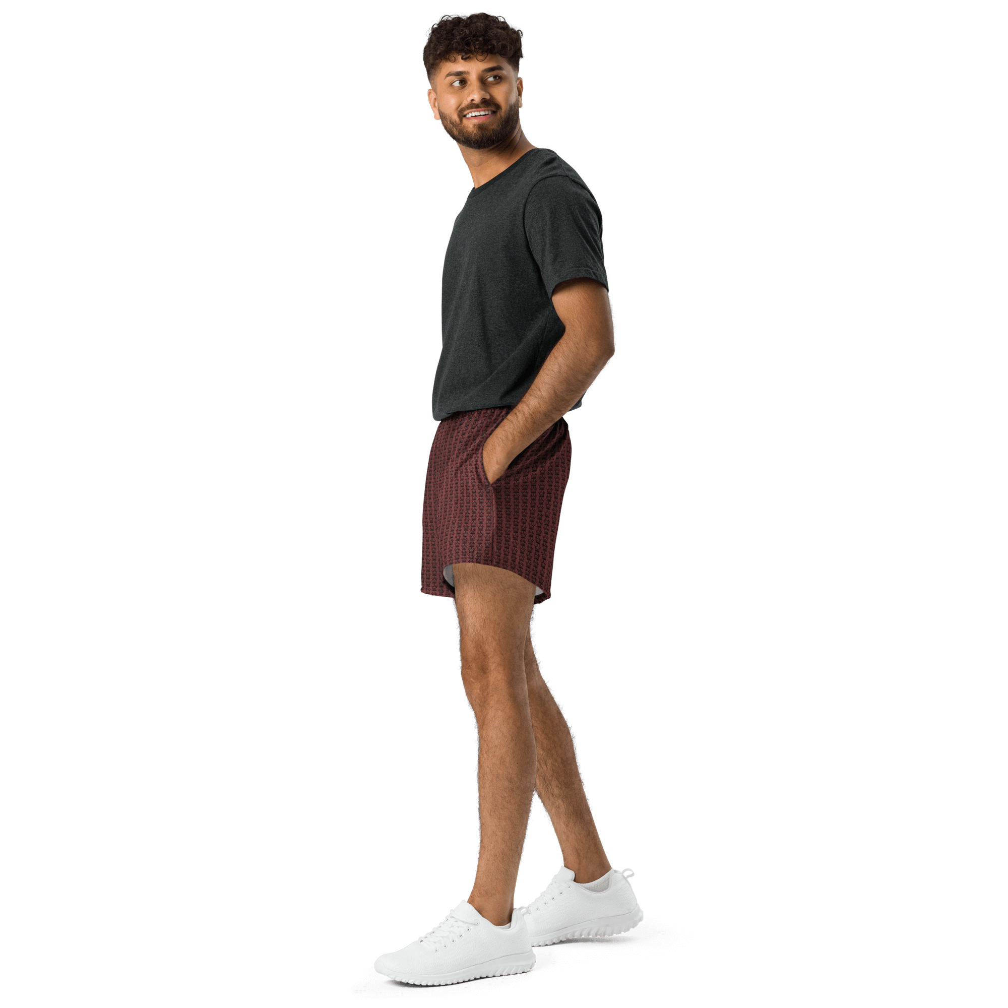 A man in a gray t-shirt and patterned maroon shorts poses in white sneakers against a black background.