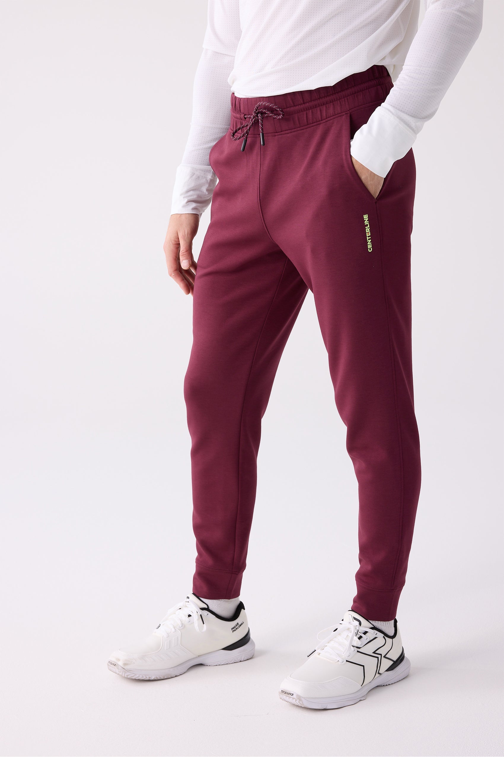 Maroon Men's Après Jogger by Centerline Athletics, with an elastic waist, drawstring, and vertical logo, worn with a white long-sleeve shirt and white sneakers.