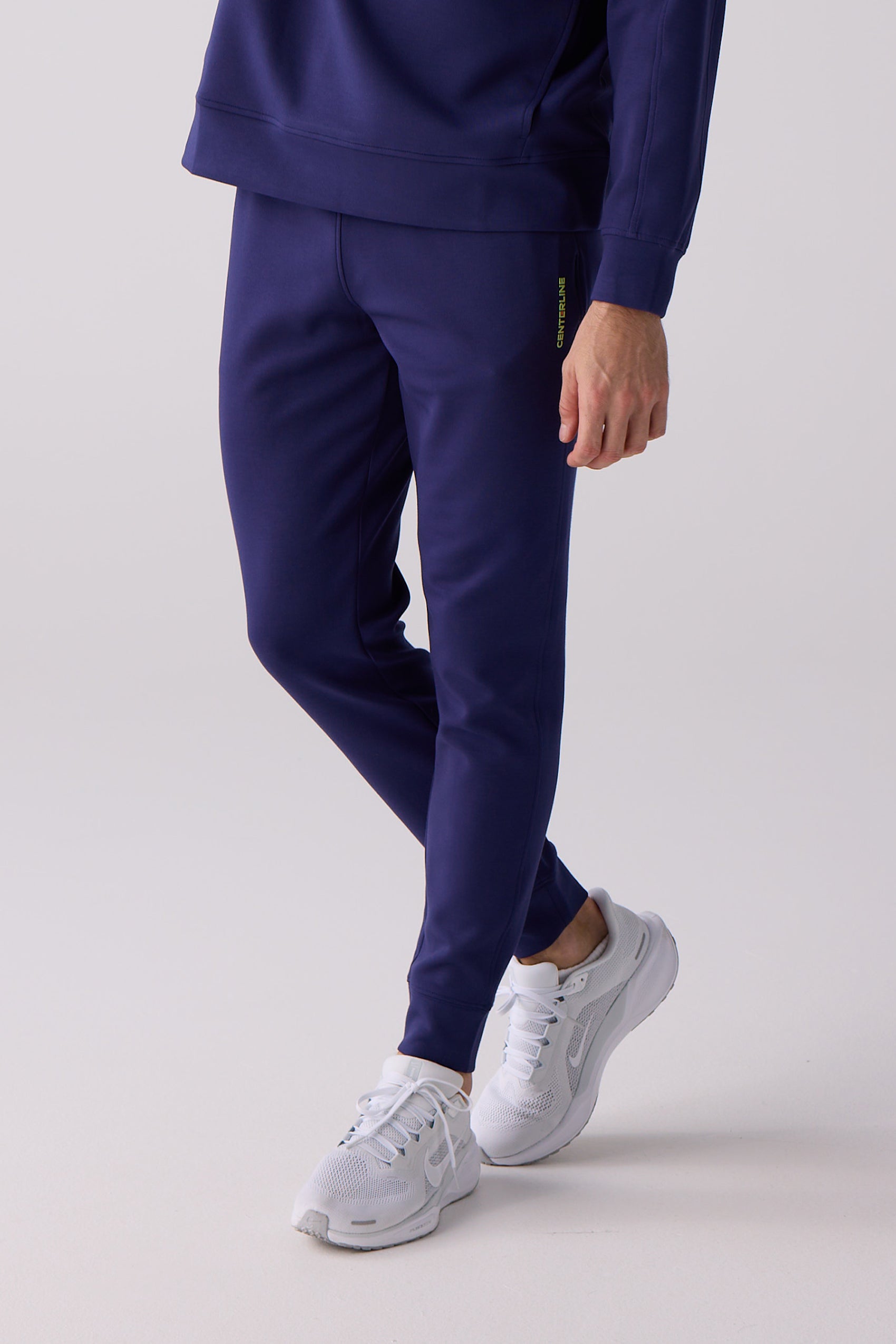 Navy blue men's jogger by Centerline Athletics, featuring a lime green 'CENTERLINE' logo on the thigh, tapered with elasticized cuffs, worn with white sneakers.