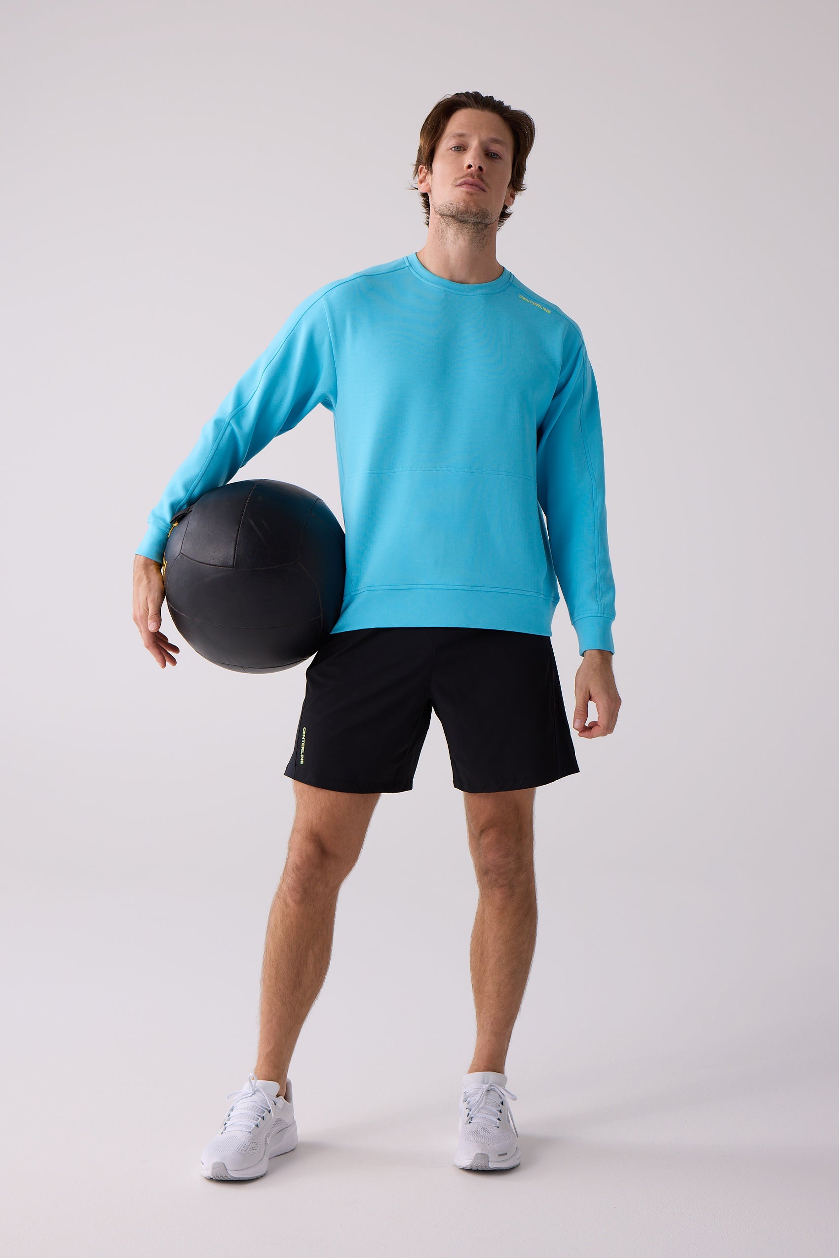 Blue crew sweatshirt by Centerline Athletics featuring yellow brand text, worn with black shorts, white athletic shoes, and a medicine ball.