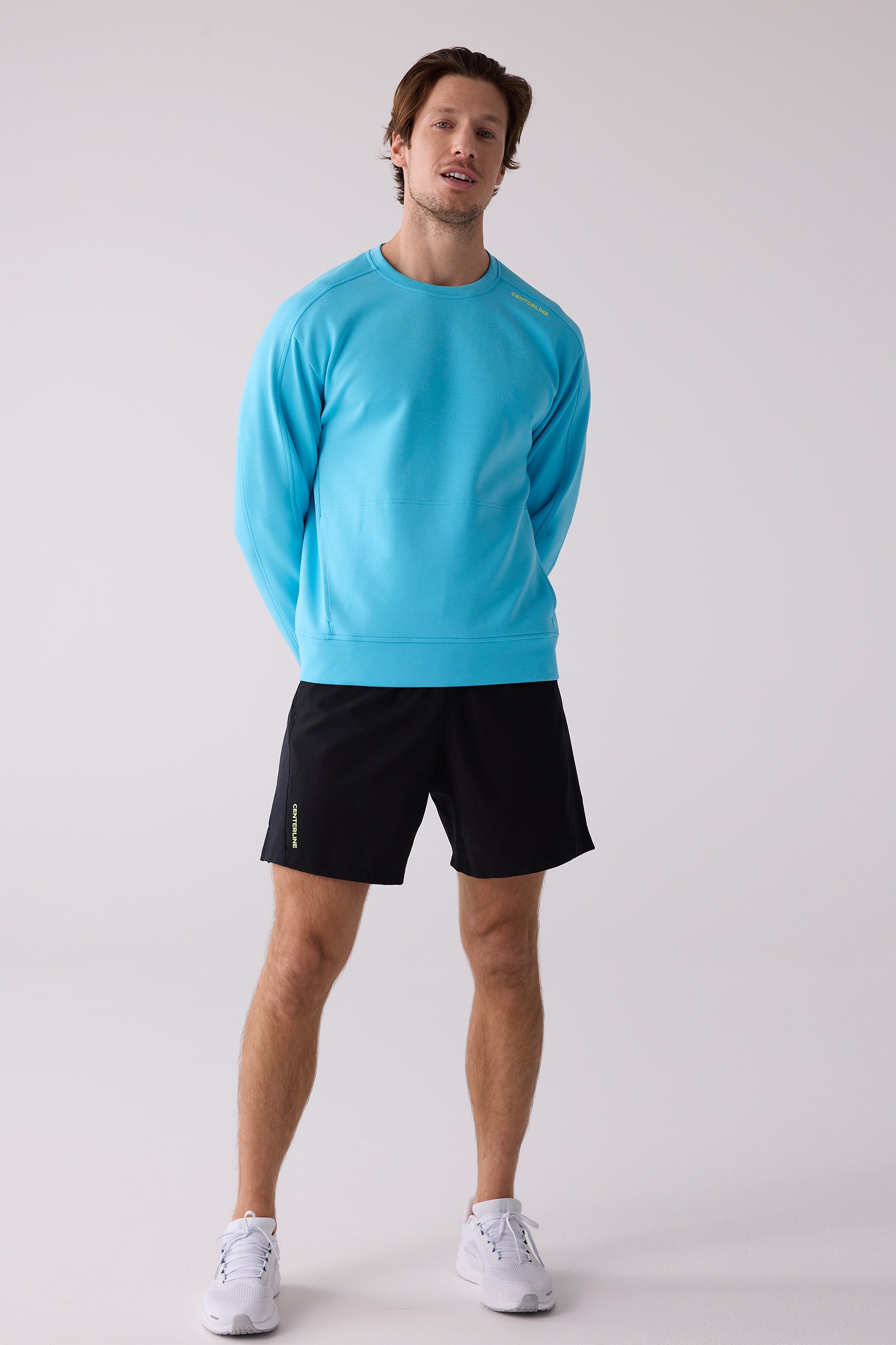 Bright blue men's crew sweatshirt by Centerline Athletics featuring yellow shoulder text, worn with black shorts and white sneakers.