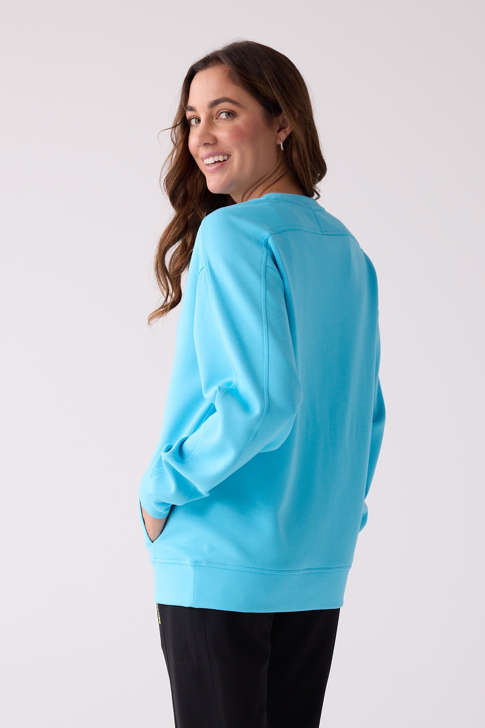 Sky blue women's crew sweatshirt by Centerline Athletics, with visible stitching, ribbed cuffs and hem, shown from a back angle with hands in pockets.