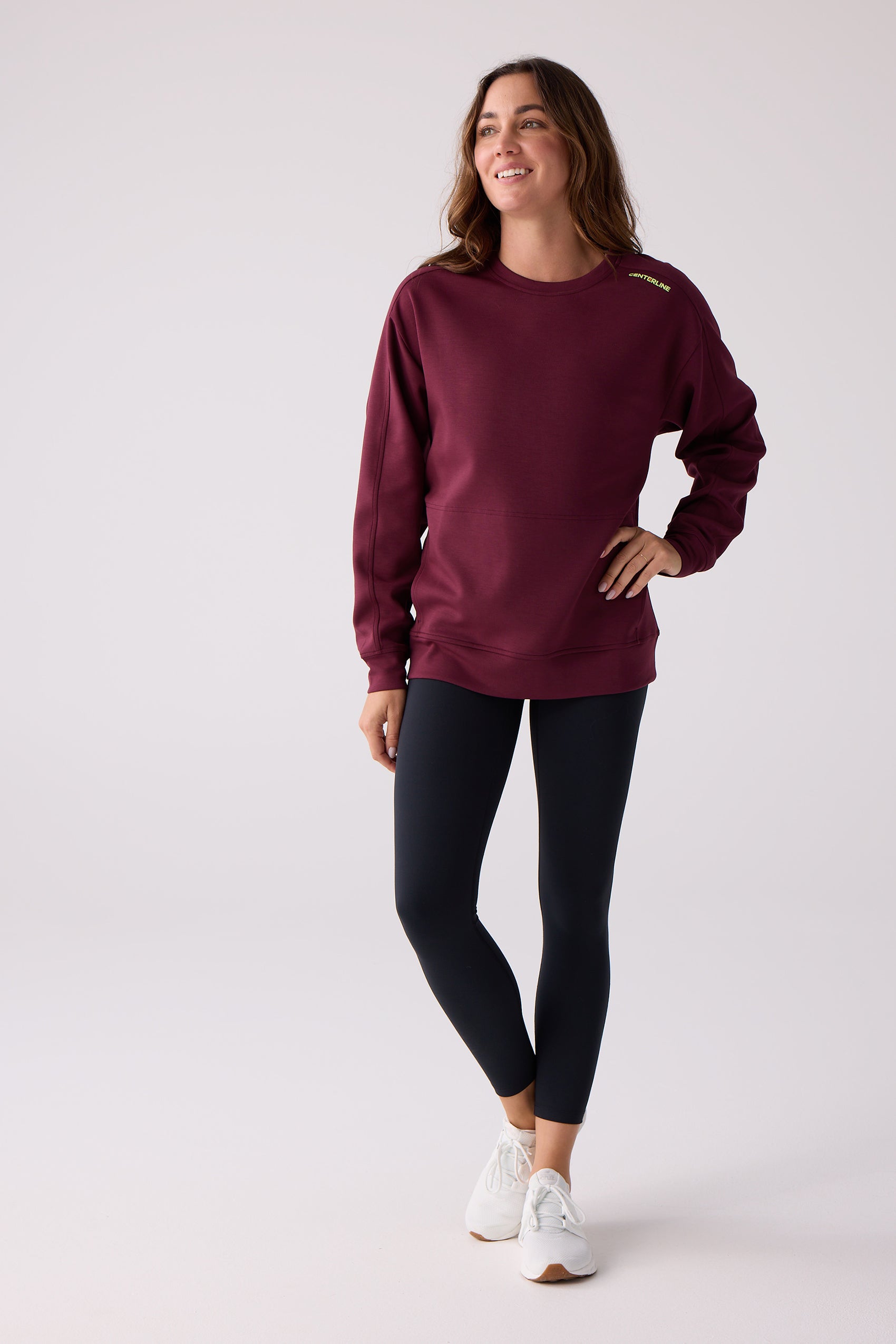 Women's burgundy crew sweatshirt by Centerline Athletics, with yellow 'CENTERLINE' text on the shoulder, worn with black leggings and white sneakers.