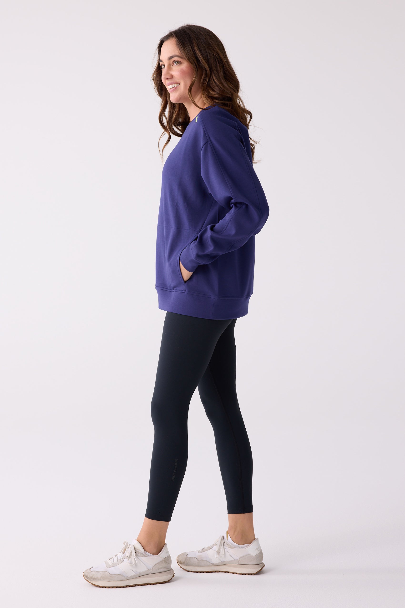 Side view of a purple women's crew sweatshirt by Centerline Athletics, featuring pockets and a subtle logo, worn with black leggings.