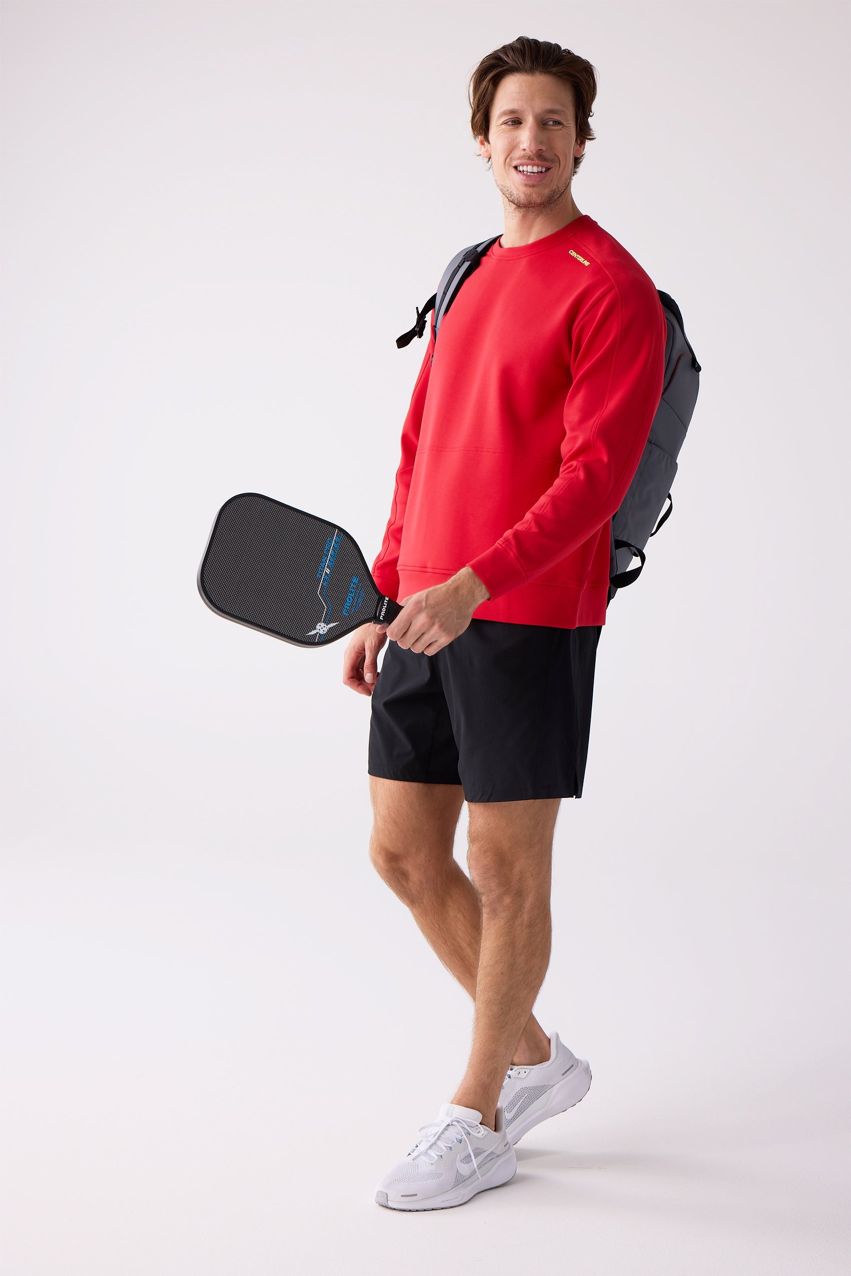 Red men's crew sweatshirt by Centerline Athletics, featuring a yellow shoulder logo, worn by a man with black shorts, white shoes, and a pickleball paddle.