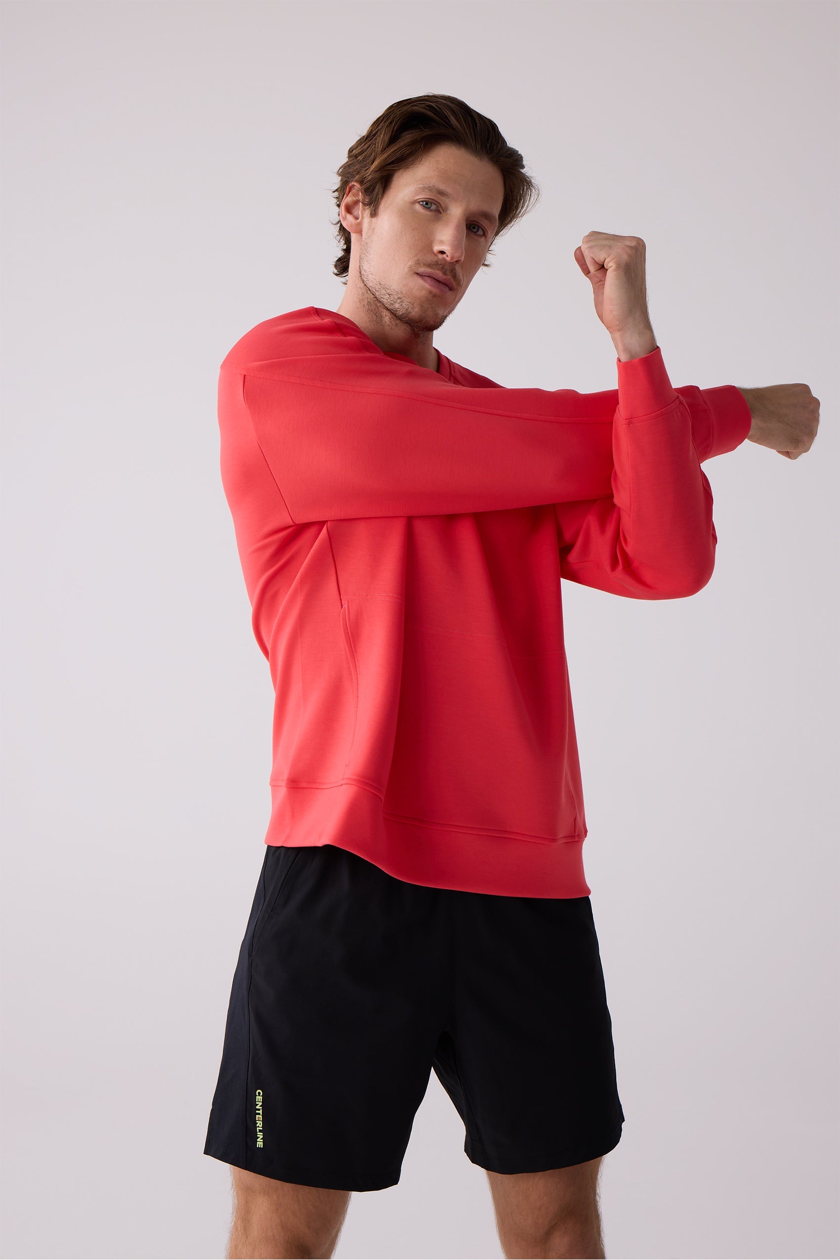 Red men's crew sweatshirt by Centerline Athletics, worn by a man stretching and paired with black shorts.