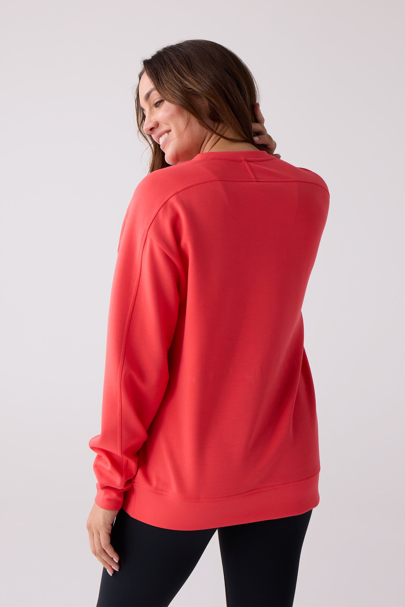 Coral crew sweatshirt by Centerline Athletics, with ribbed cuffs and hem, on a woman wearing black leggings, back and side view.