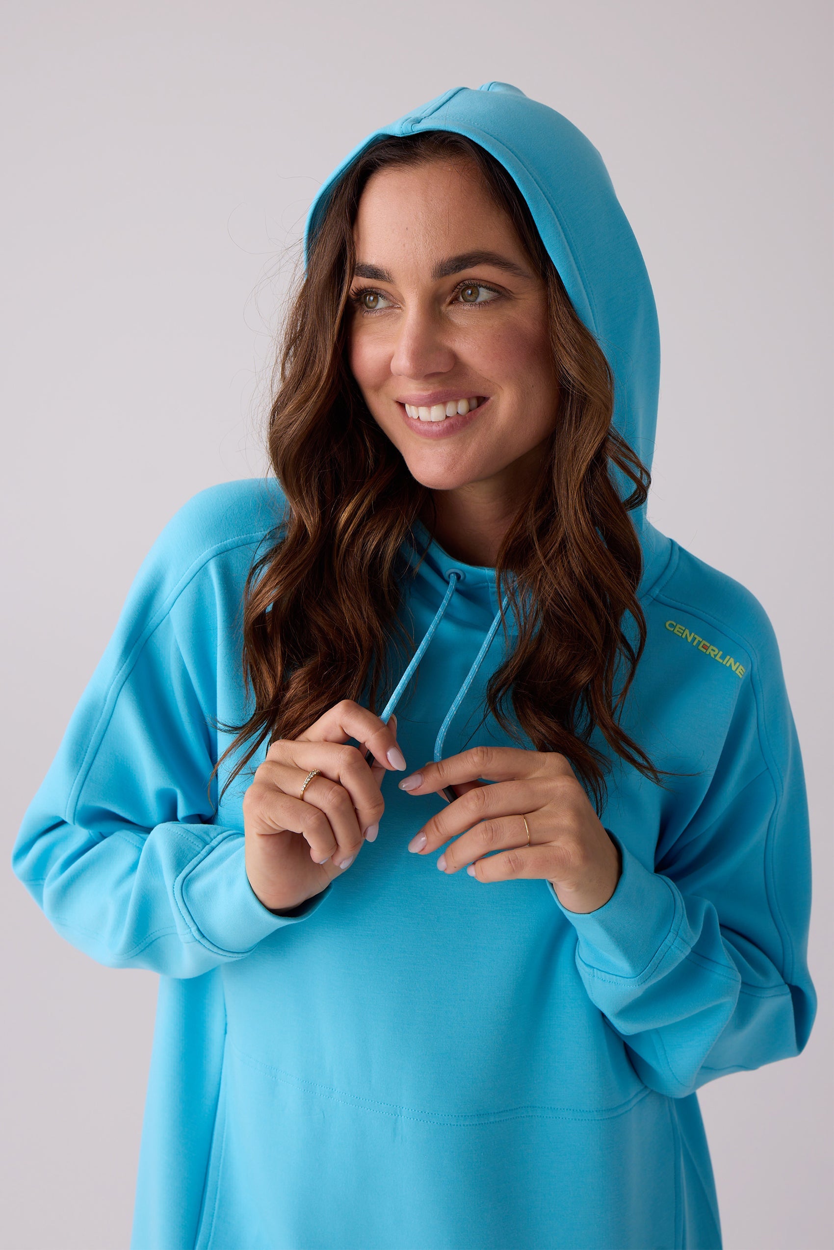 Blue hooded sweatshirt by Centerline Athletics, with yellow 'CENTERLINE' text on the shoulder, worn by a smiling woman holding drawstrings.