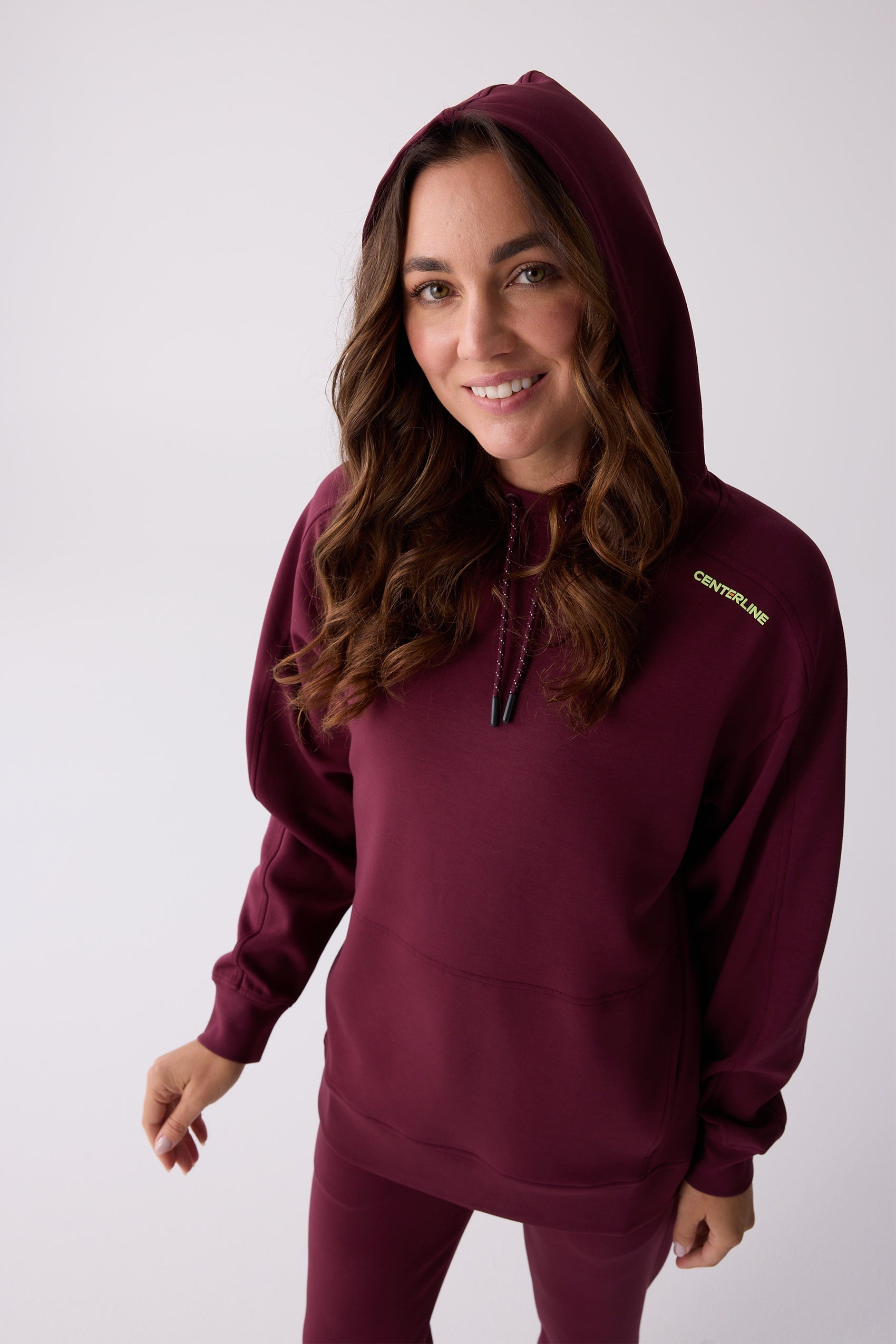 Maroon hooded sweatshirt by Centerline Athletics with a lime green logo and speckled drawstrings, worn by a smiling woman in matching pants.