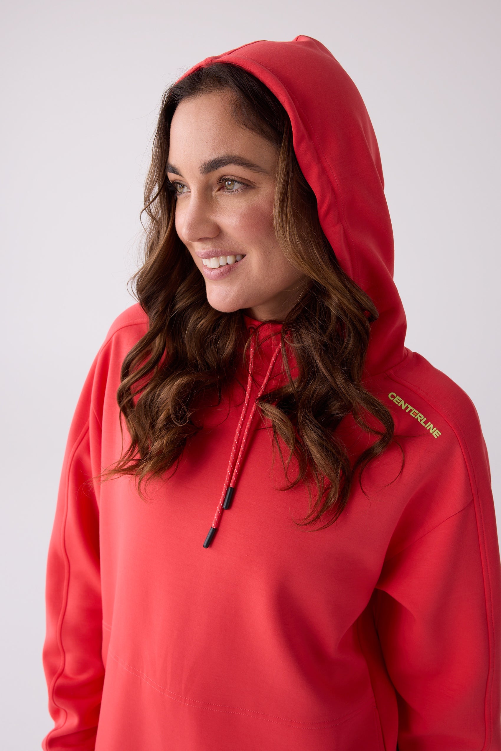 Red hooded sweatshirt by Centerline Athletics, with chartreuse logo on shoulder, drawstrings, worn by a smiling woman.