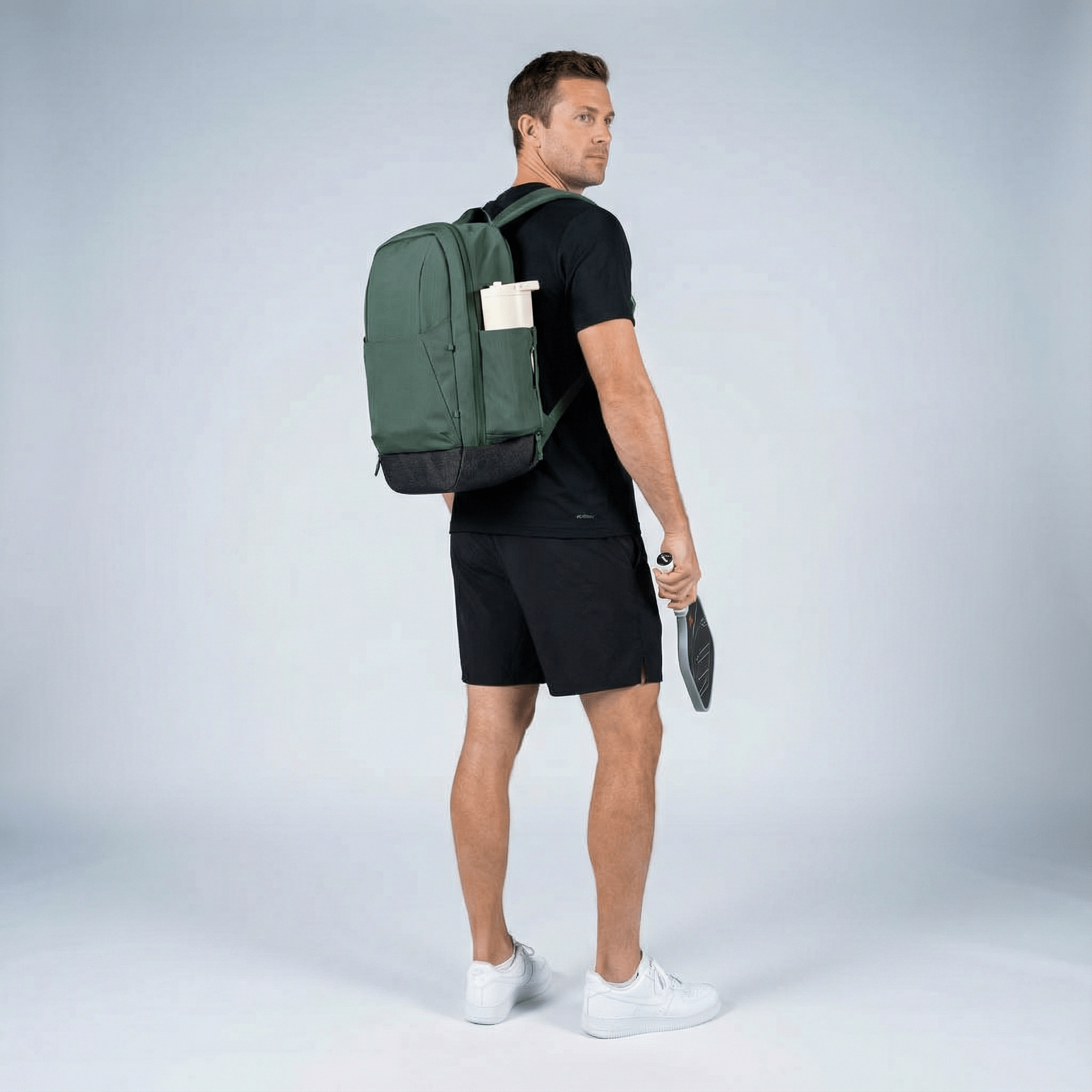 Green pickleball backpack by FORWRD, worn by a man holding a paddle, with a water bottle in its side pocket.