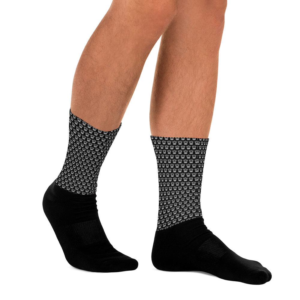 Two legs wearing black socks with a pattern of white crowns. 
