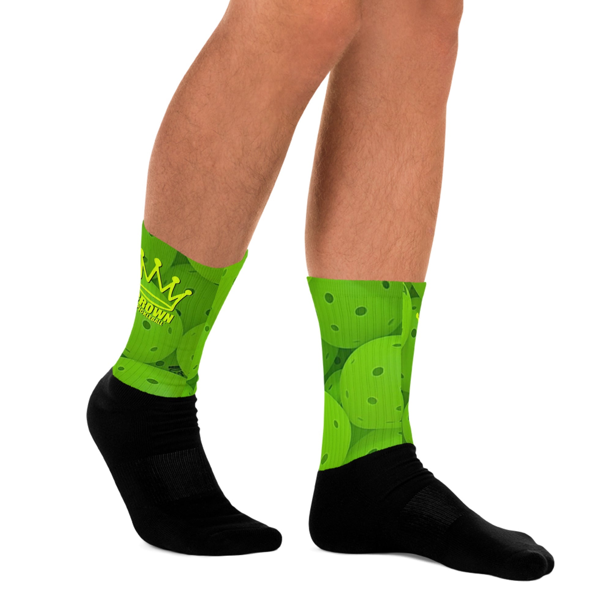 Pair of legs wearing green pickleball patterned socks with black feet.