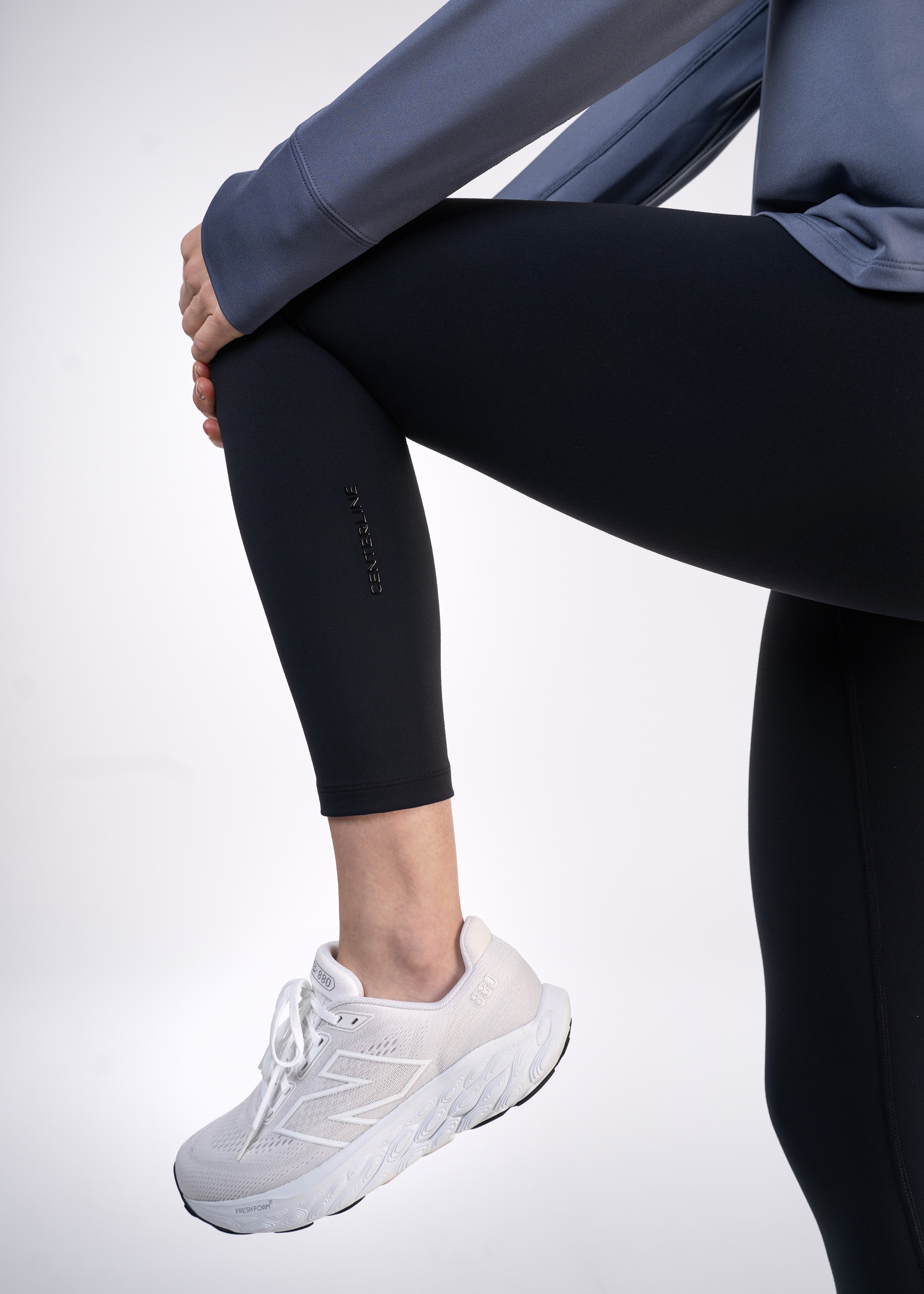 A person in black leggings and white sneakers, stretching.