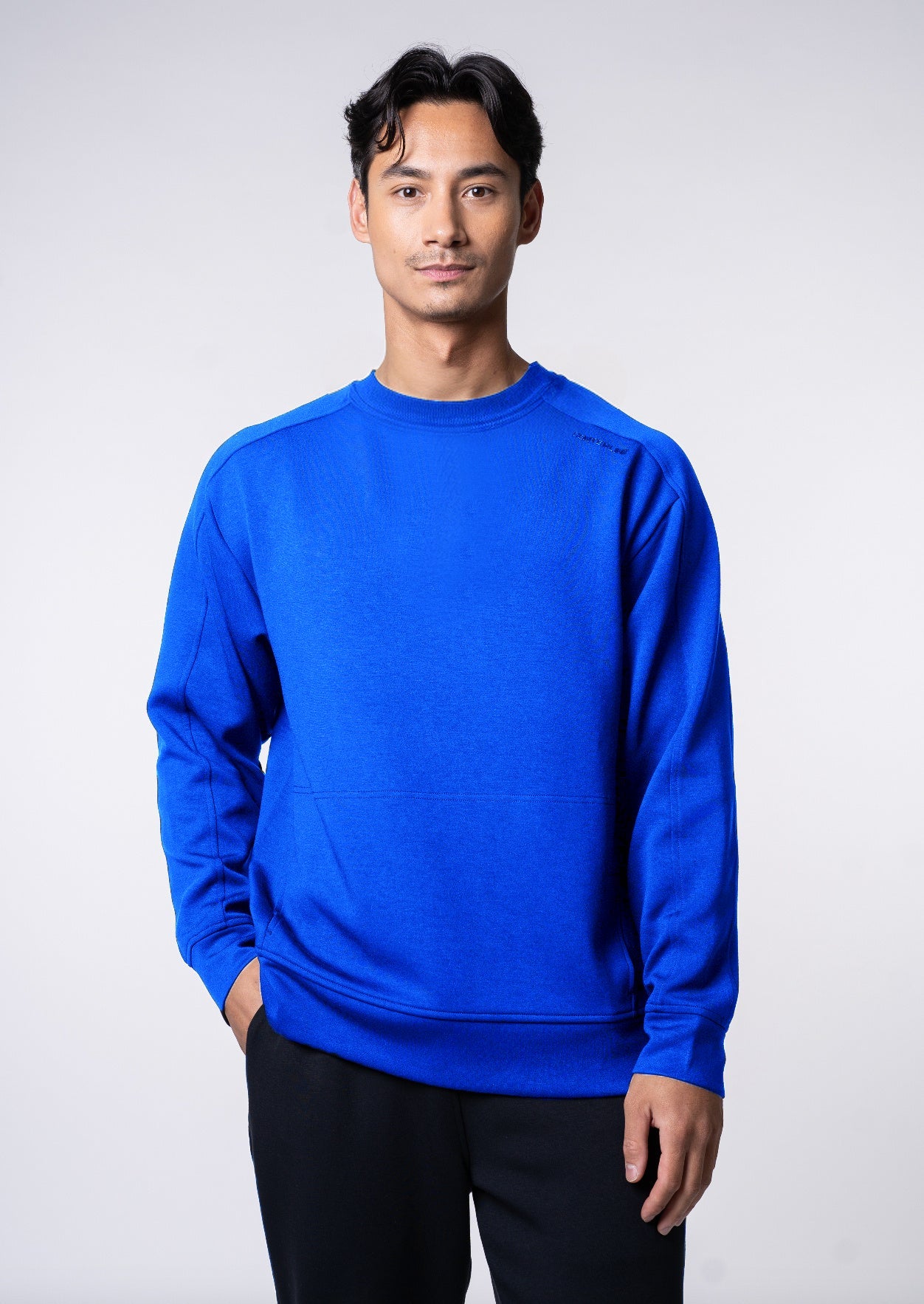 Man in blue sweatshirt with black pants and hand in pocket.