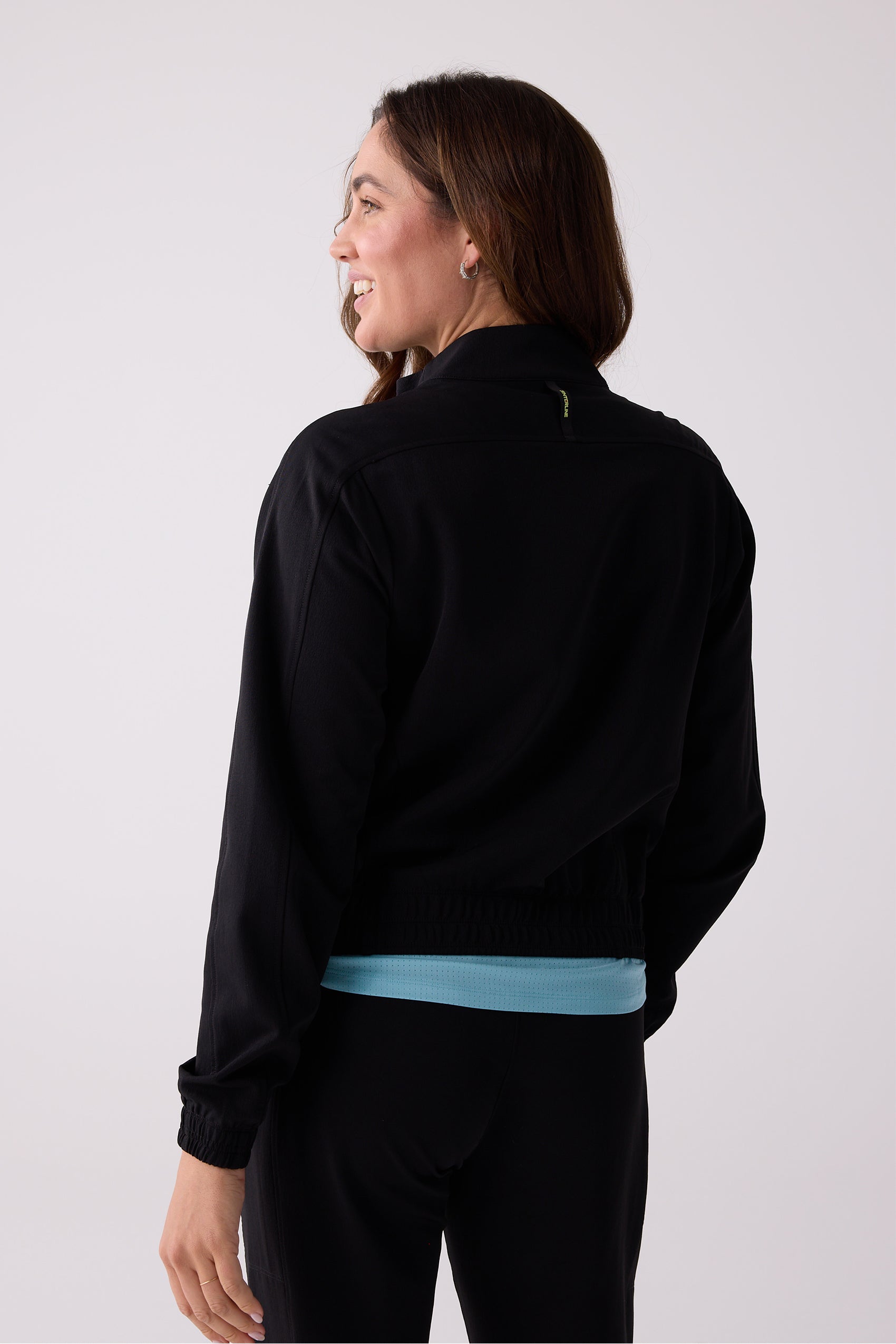 Black Women's Courtside Track Jacket by Centerline Athletics, back view with high collar, elasticized hem, and green tag.