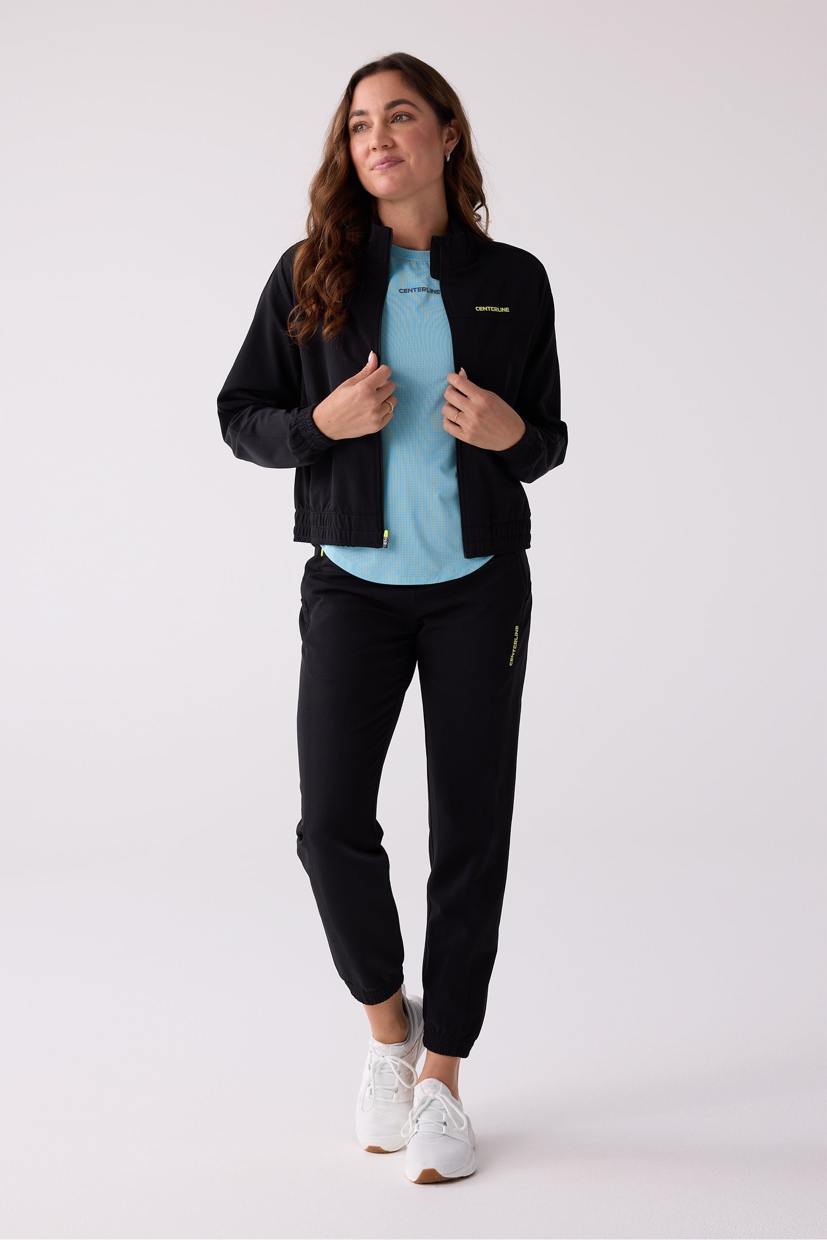 Black Women's Courtside Track Jacket by Centerline Athletics with yellow branding, styled open over a light blue t-shirt and black track pants.