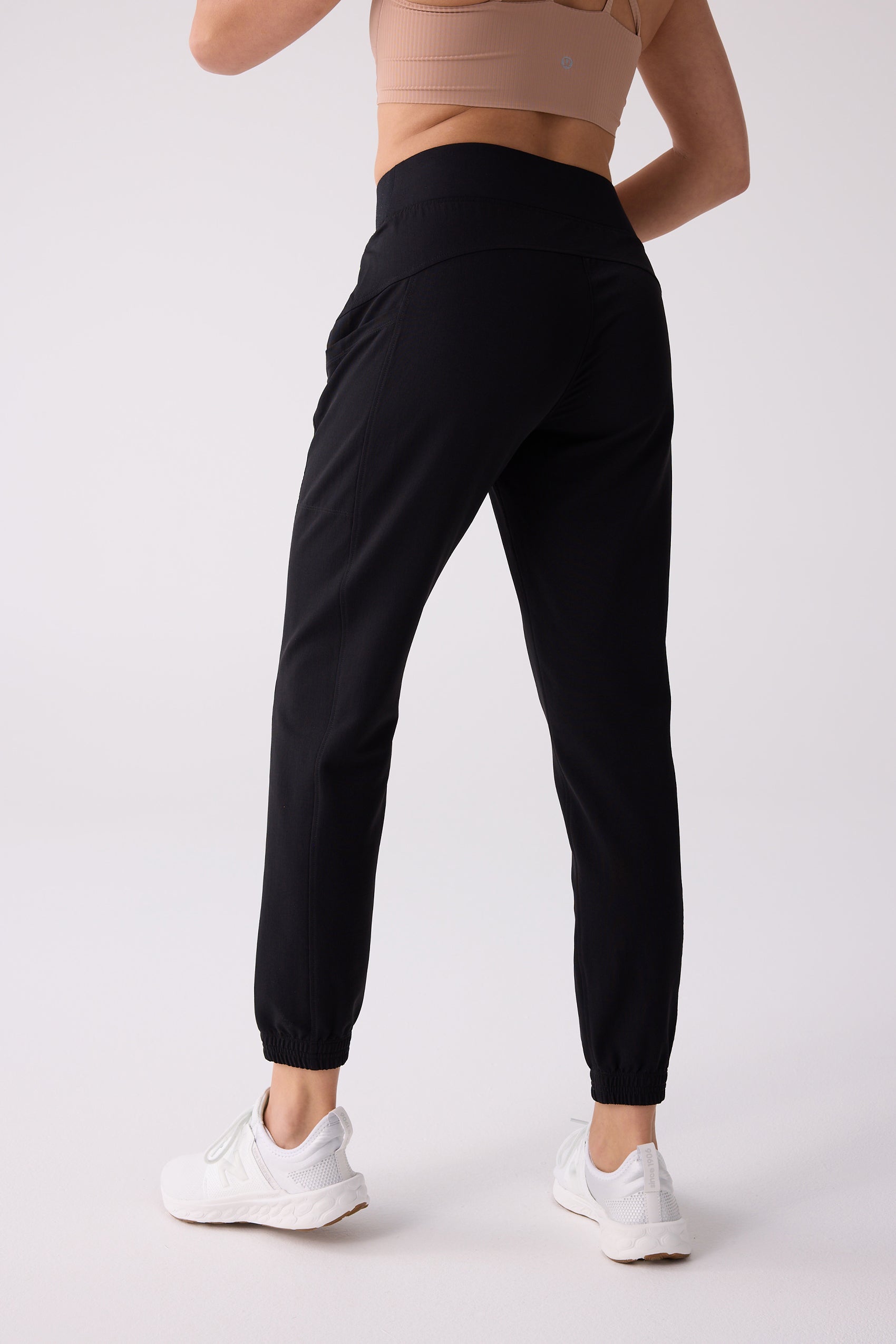 Black jogger track pants by Centerline Athletics, shown from the back with a nude sports bra and white sneakers.