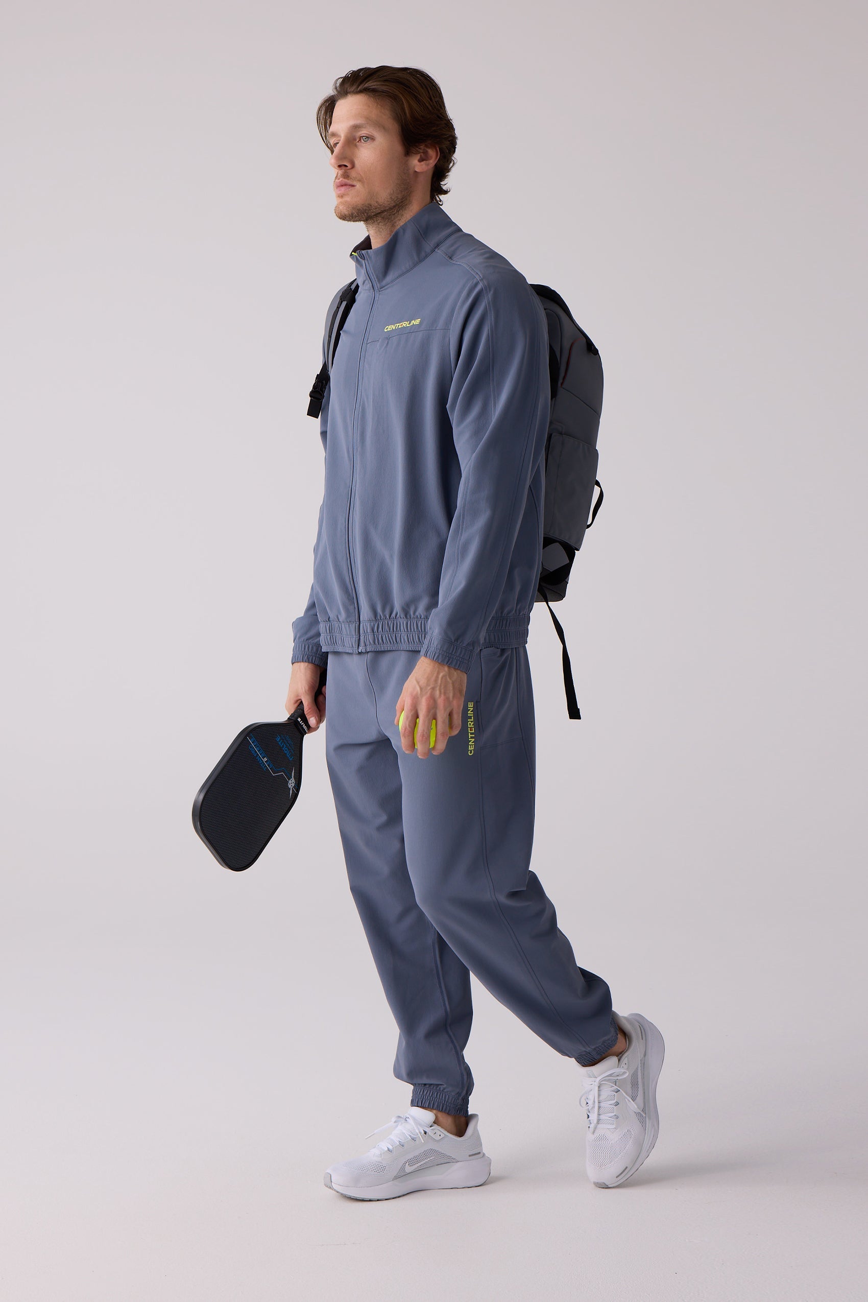 Dusty blue track pants with elastic cuffs by Centerline Athletics, featuring yellow CENTERLINE text, worn by a man holding a pickleball paddle and ball.