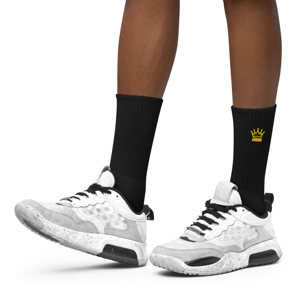 A person wearing black socks with a gold crown and white sneakers.