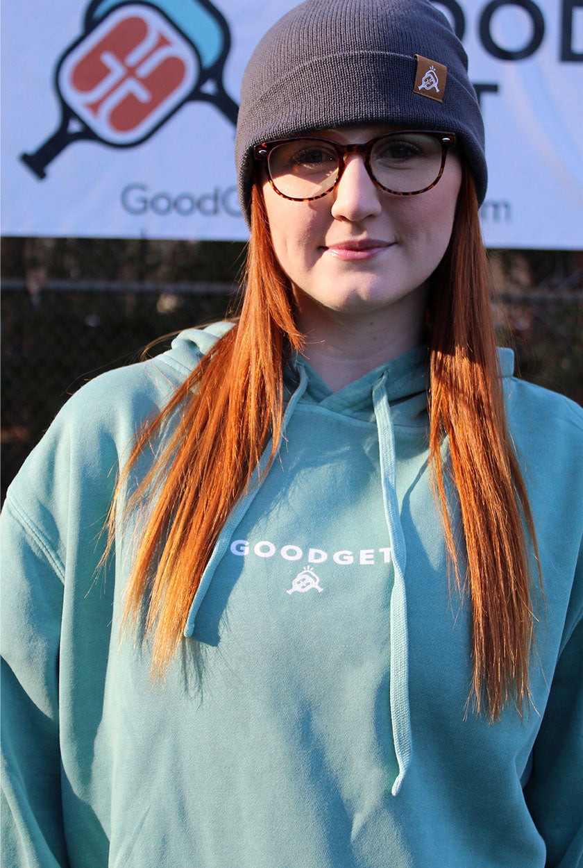 Light teal men's hoodie by Good Get, with white logo print on chest, worn by a woman with red hair and a gray beanie.