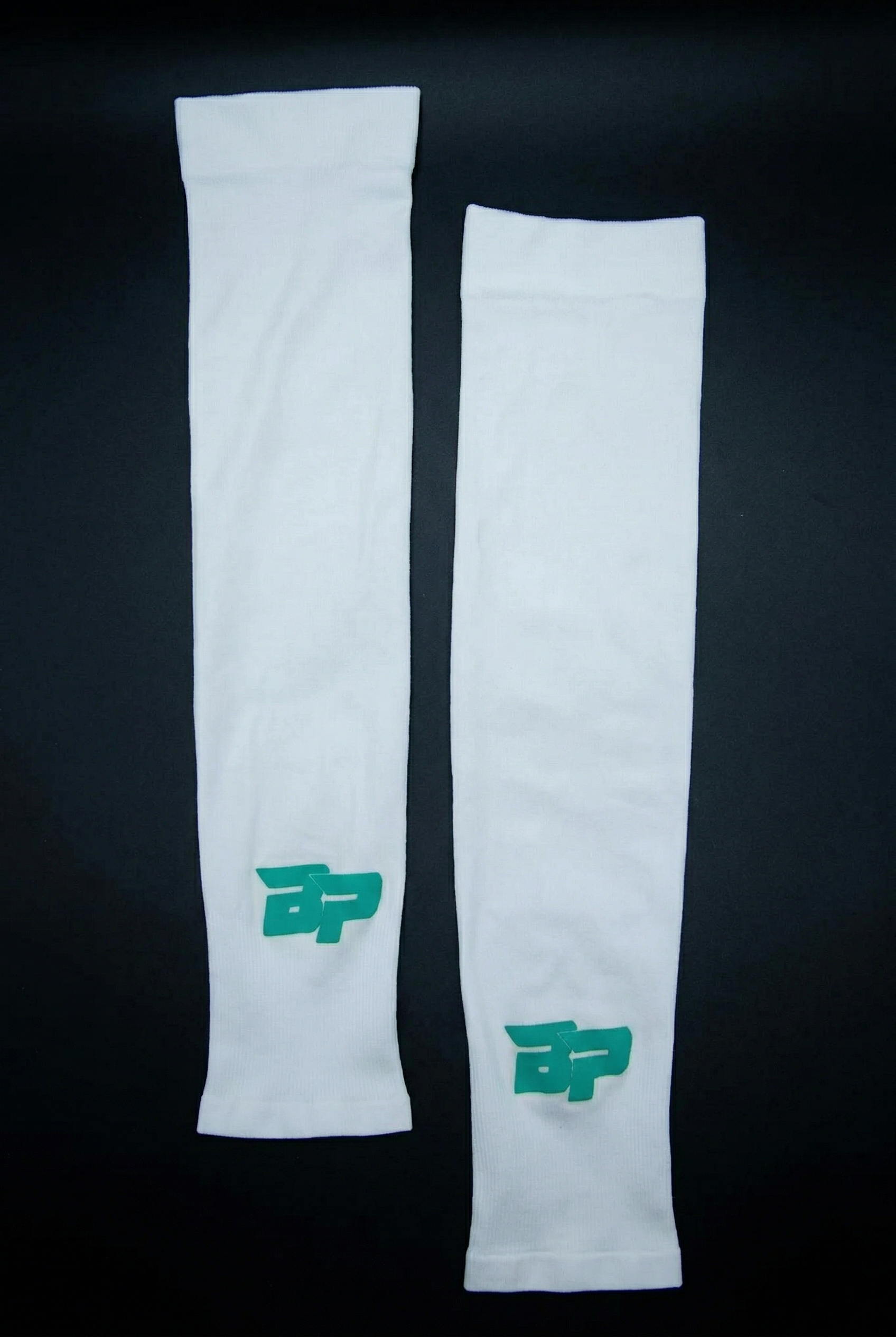 White arm sleeves by Bodhi Pickleball, featuring a green BP logo on each, laid flat on a dark background.