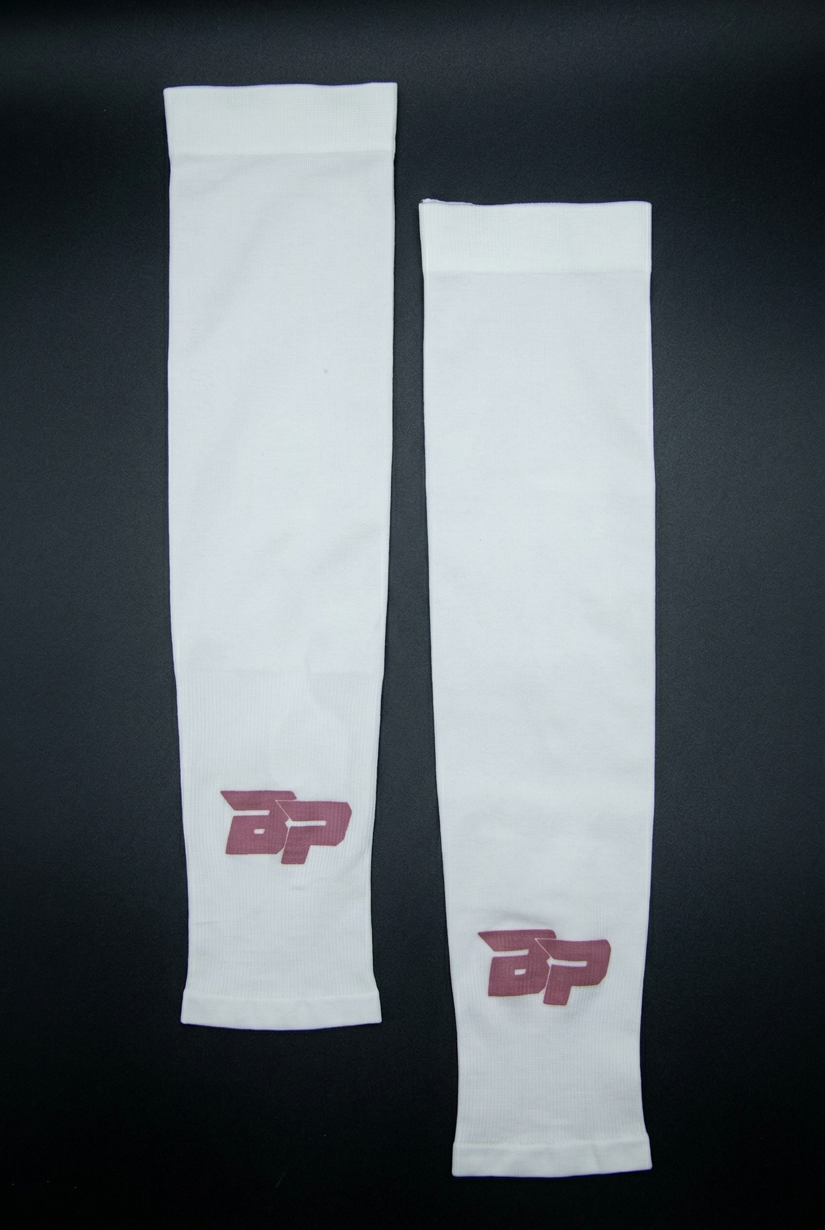 Two white Performance Arm Sleeves by Bodhi Pickleball, with dark red 'BP' logos, laid flat on a dark background.