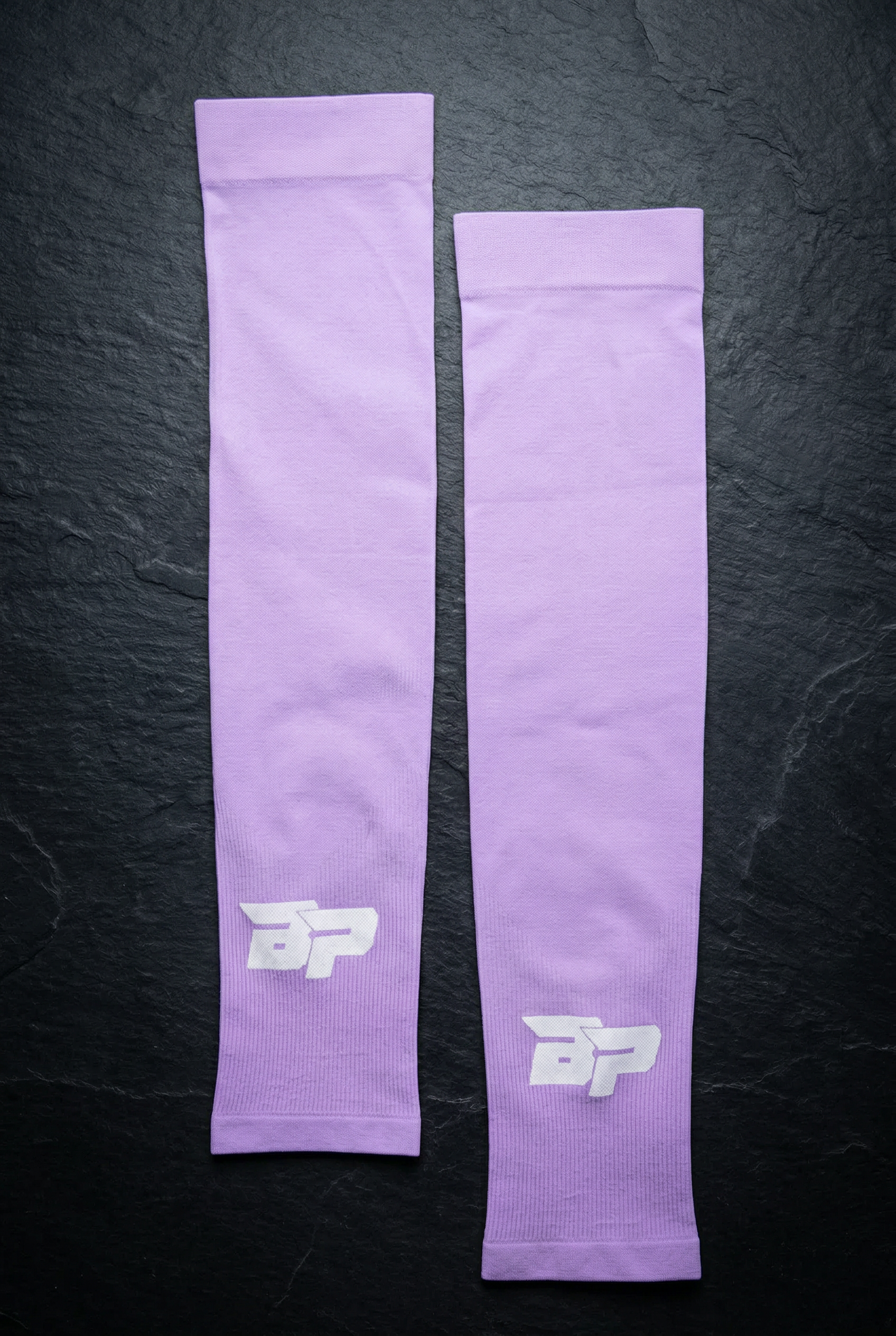 Lavender ribbed arm sleeves by Bodhi Pickleball with white "BP" logos, laid flat on a dark surface.