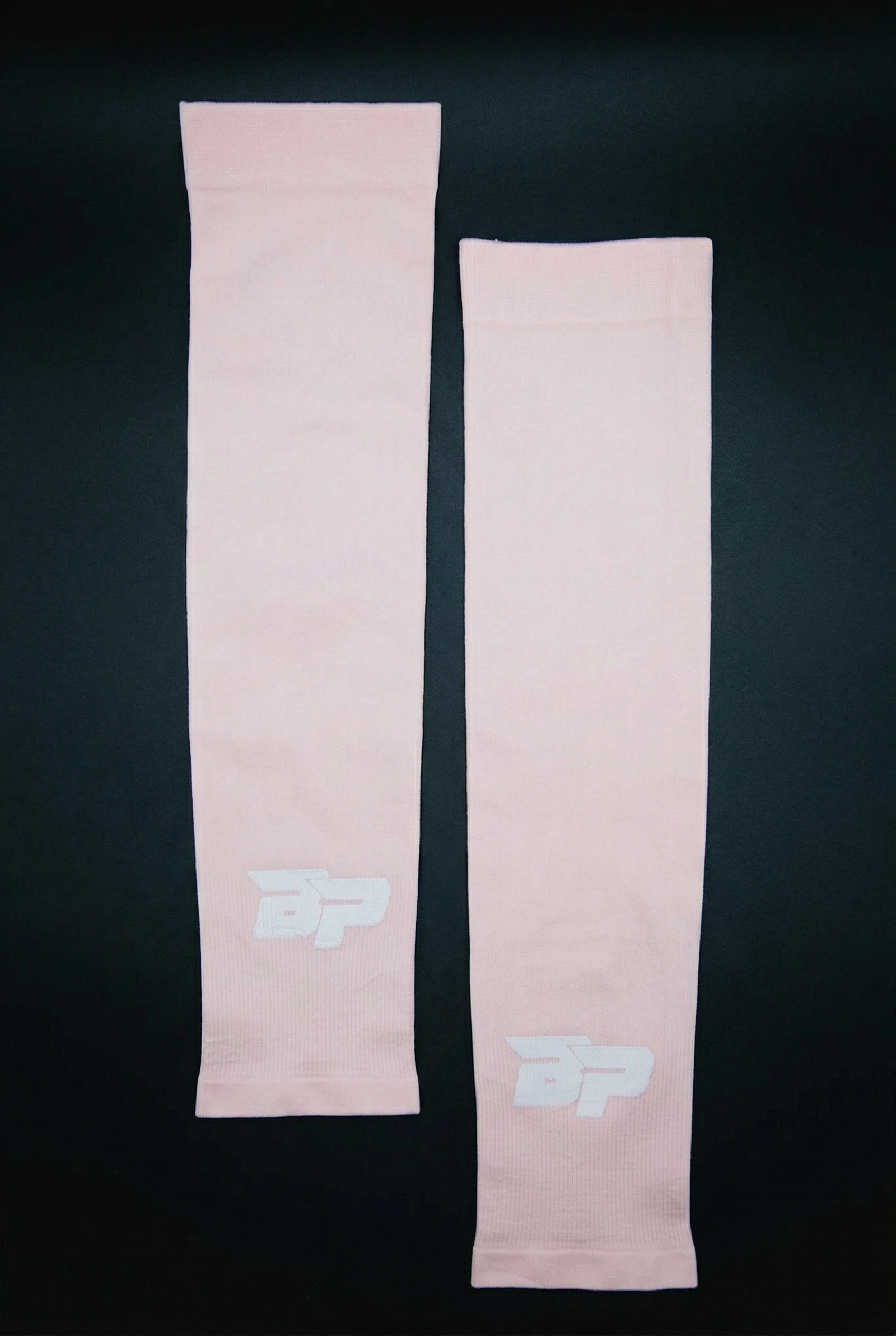 Light pink ribbed Performance Arm Sleeves by Bodhi Pickleball, each featuring a white "BP" logo, laid flat on a dark background.