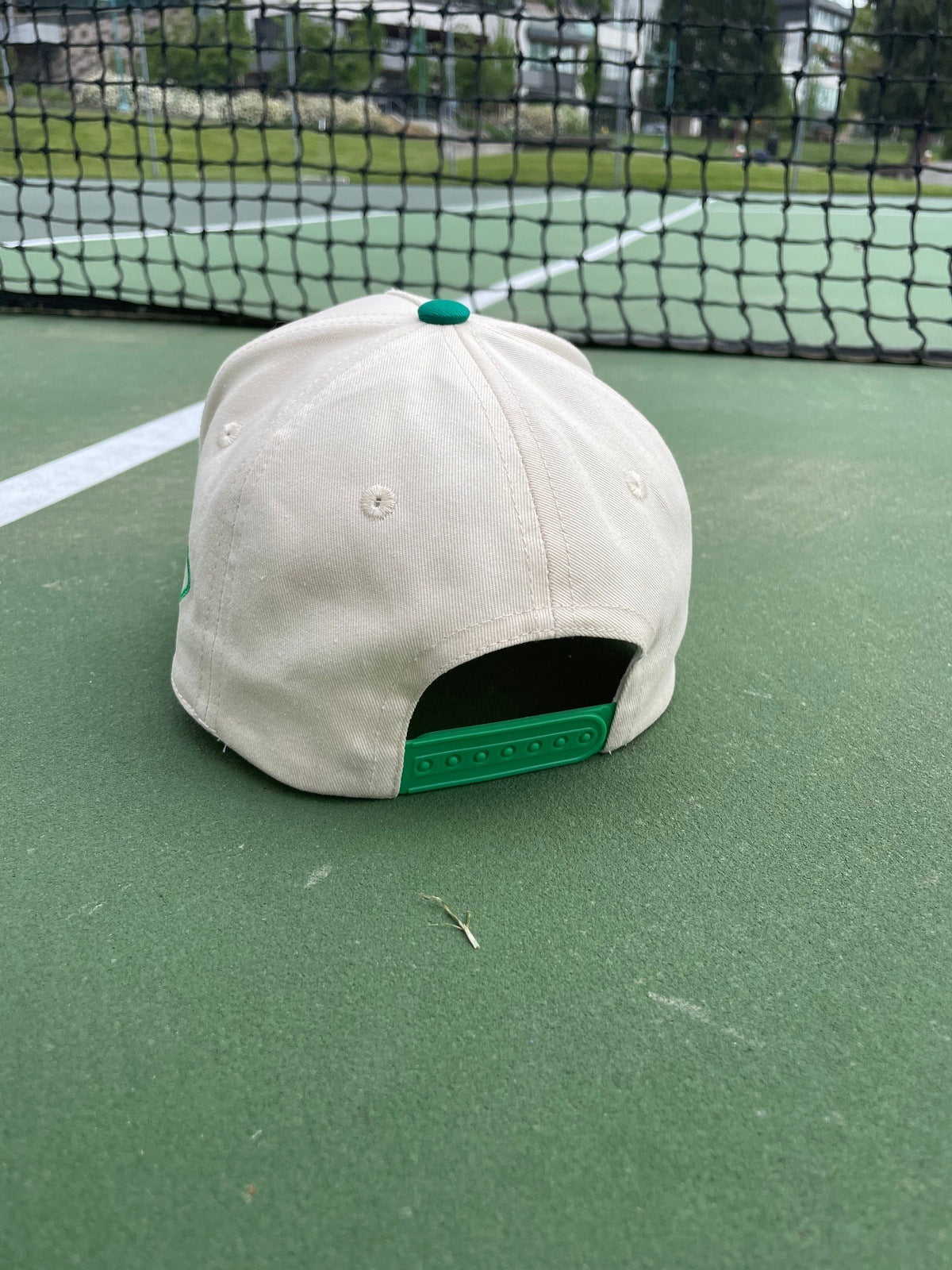 Tan and green baseball cap on a green tennis court.