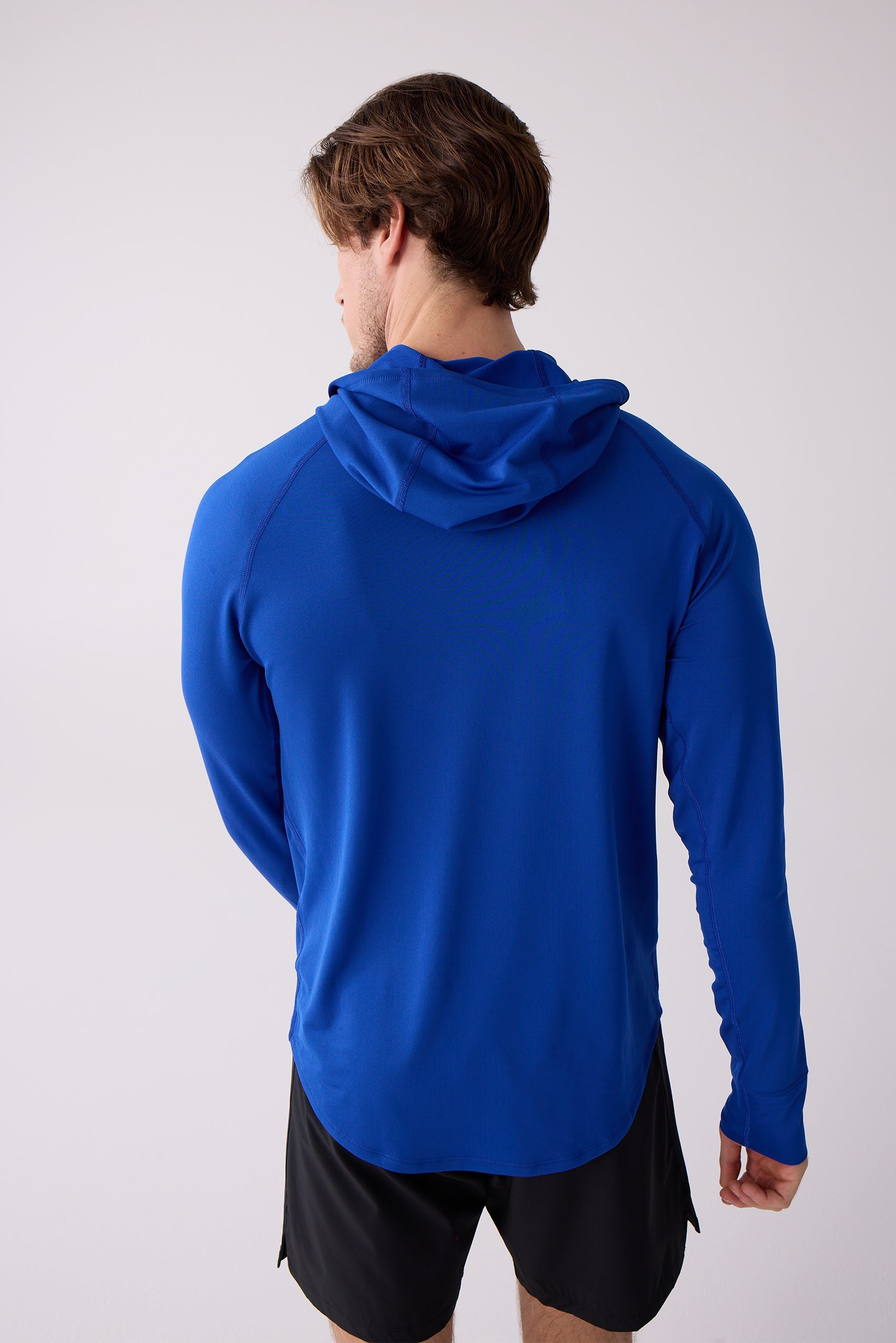 Blue men's layering hoodie by Centerline Athletics with long raglan sleeves and a hood, worn with black shorts, viewed from the back.