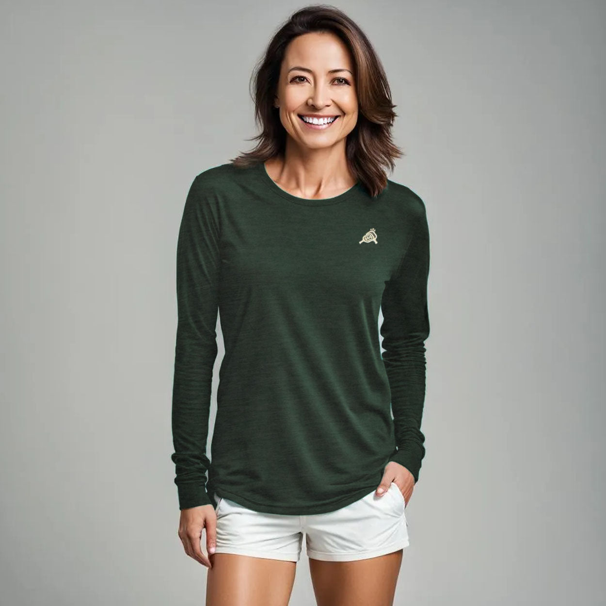 Dark green unisex long sleeve performance t-shirt by Good Get, with a small white chest logo, worn by a smiling woman in white shorts.