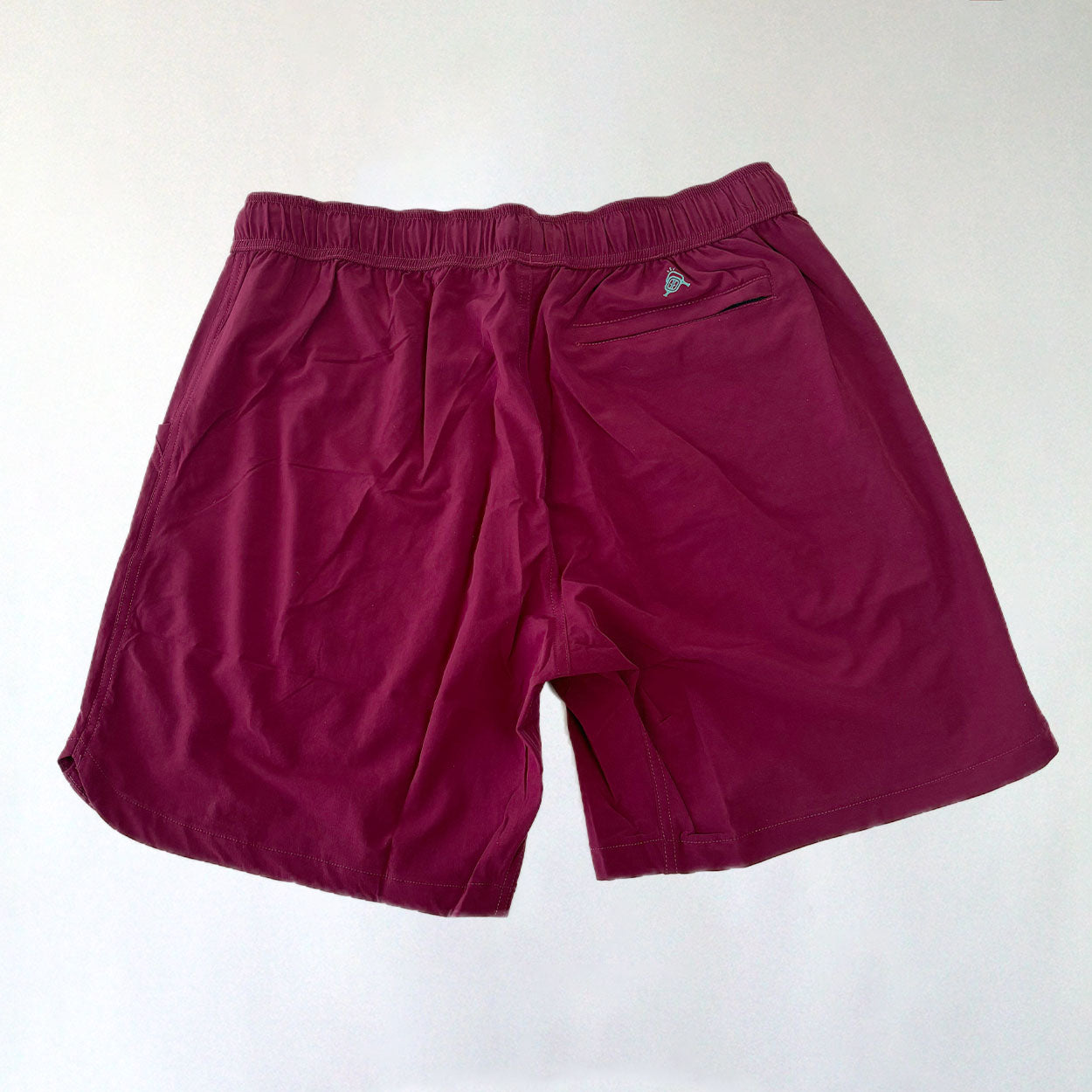 Rear view of burgundy athletic shorts with elastic waistband.
