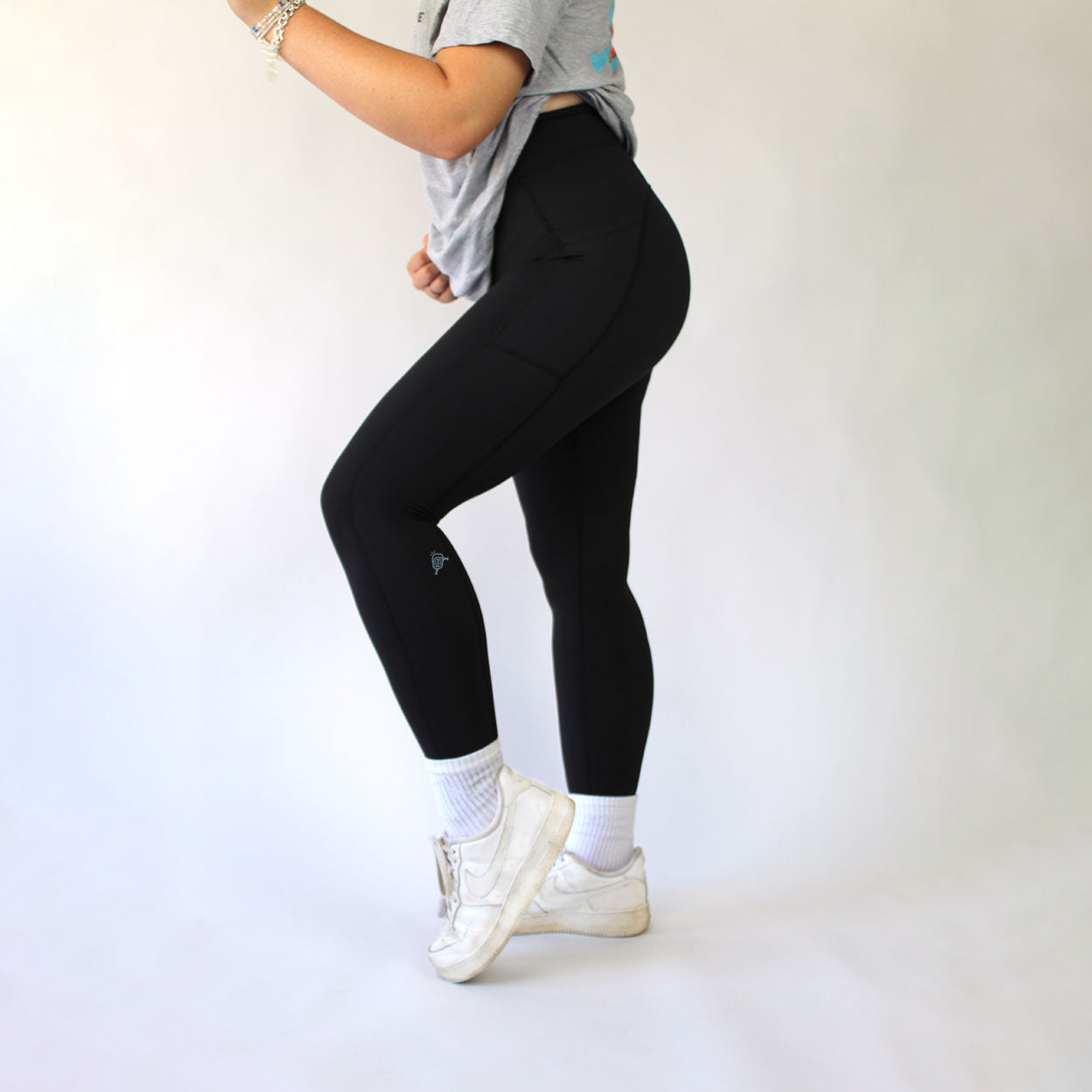 A person wearing black leggings, white socks, and white tennis shoes stands against a white background.