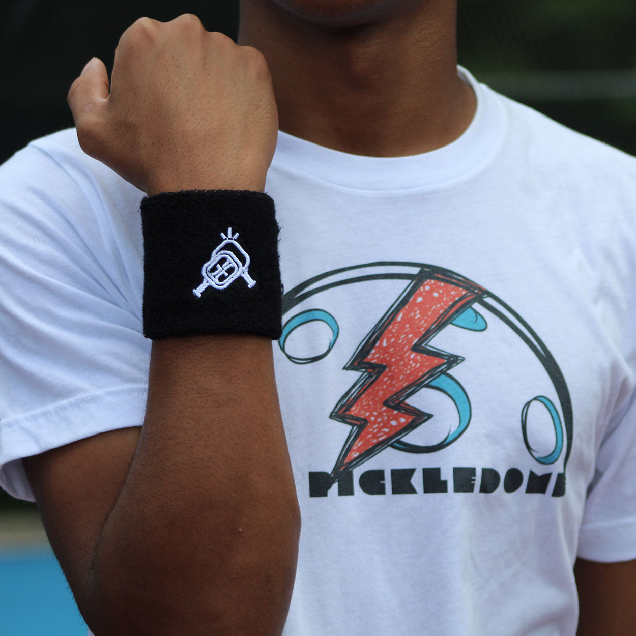 A person wearing a black wristband with a white logo and a white t-shirt with a colorful design.