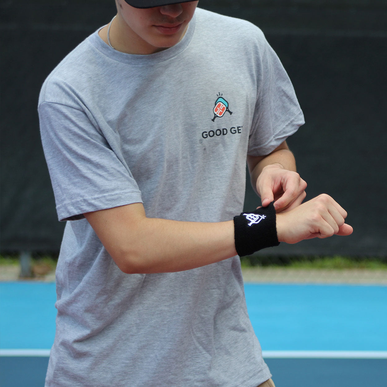 Man in gray t-shirt adjusts black wristband with white skull logo.
