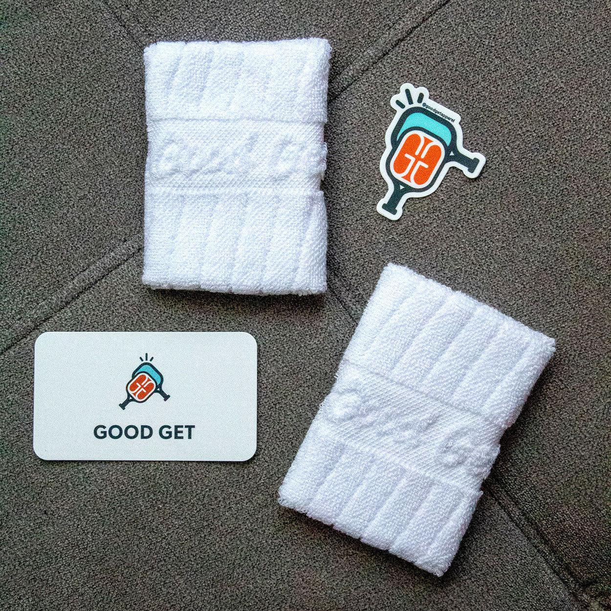 Two folded white towels, a sticker, and a business card on a gray background.