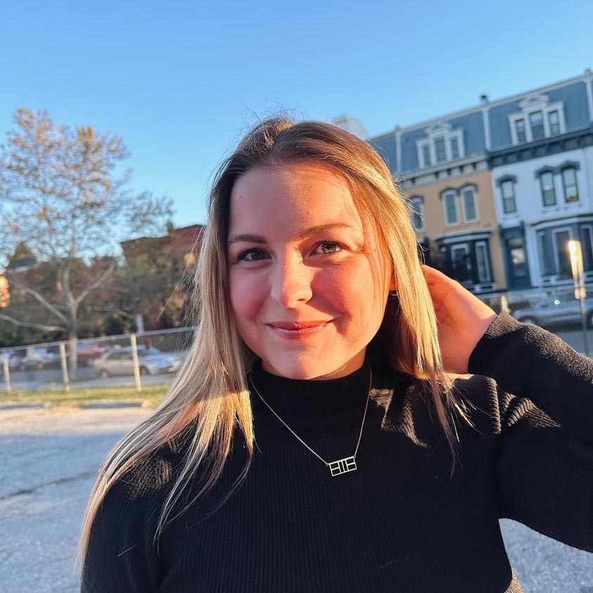 Young woman in black turtleneck, gold necklace, outdoors.