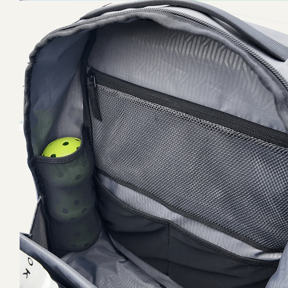 Grey Pickleball Backpack by FORWRD, showcasing its open main compartment with mesh pockets, holding two green pickleballs.