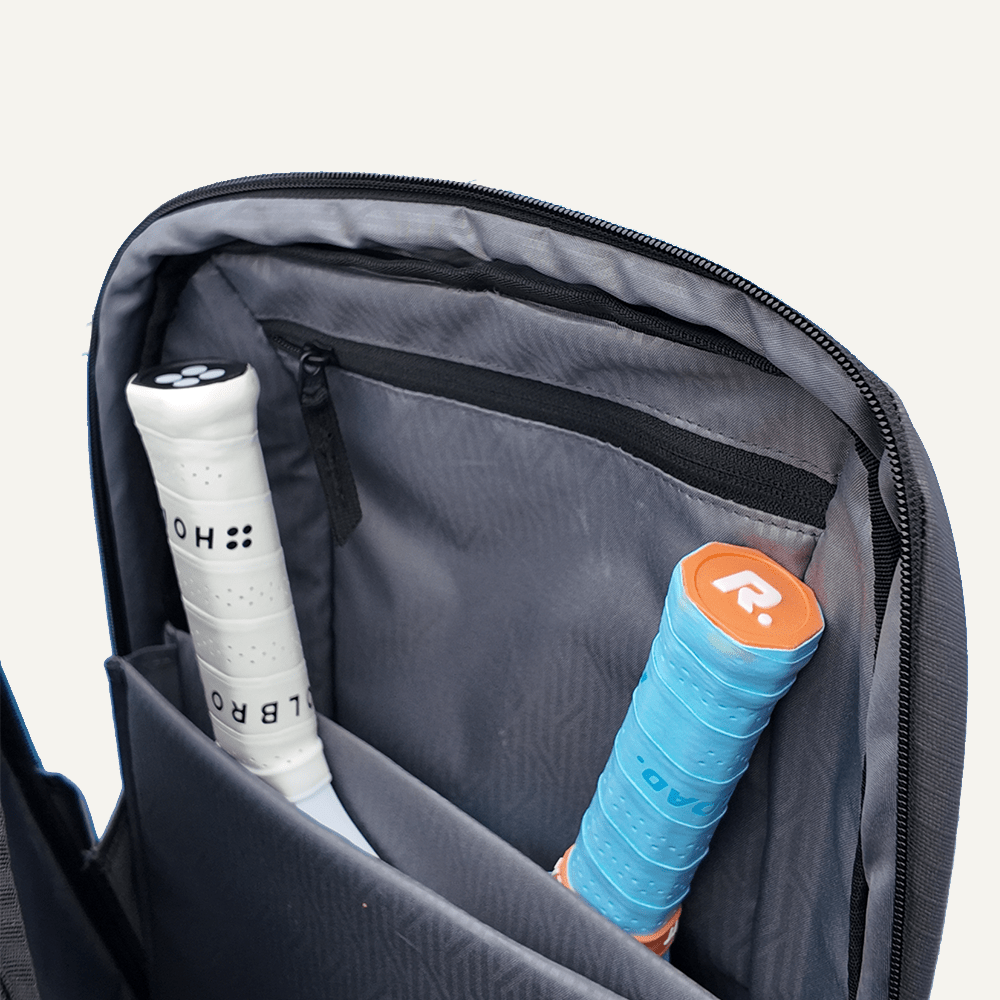 Dark grey pickleball backpack by FORWRD with an open main compartment holding two pickleball paddles.